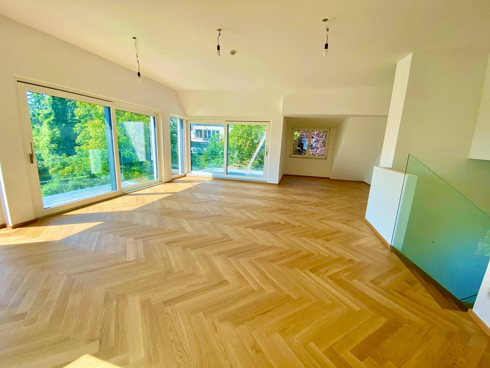 Lichtdurchfluteter Wohnbereich mit Fischgrätparkett, großen Fenstern und Blick ins Grüne.
