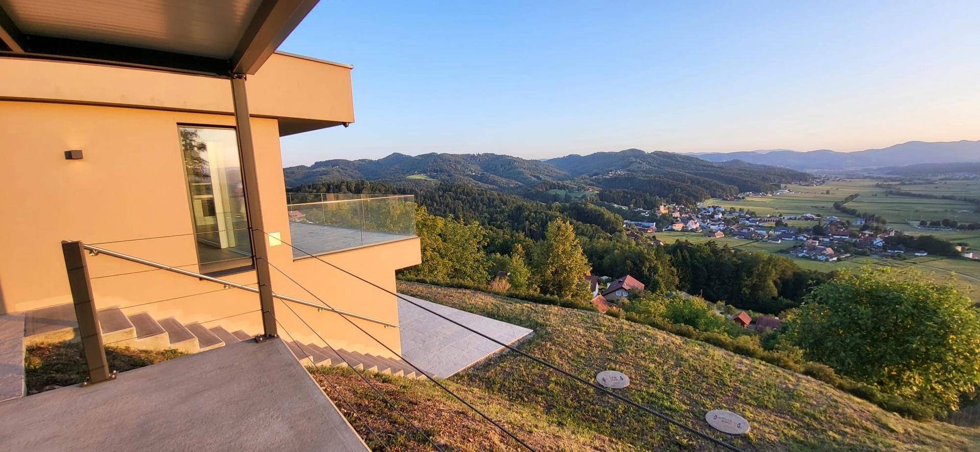 Moderne Architektur mit Außentreppe und Terrasse, umgeben von einer malerischen Hügellandschaft.