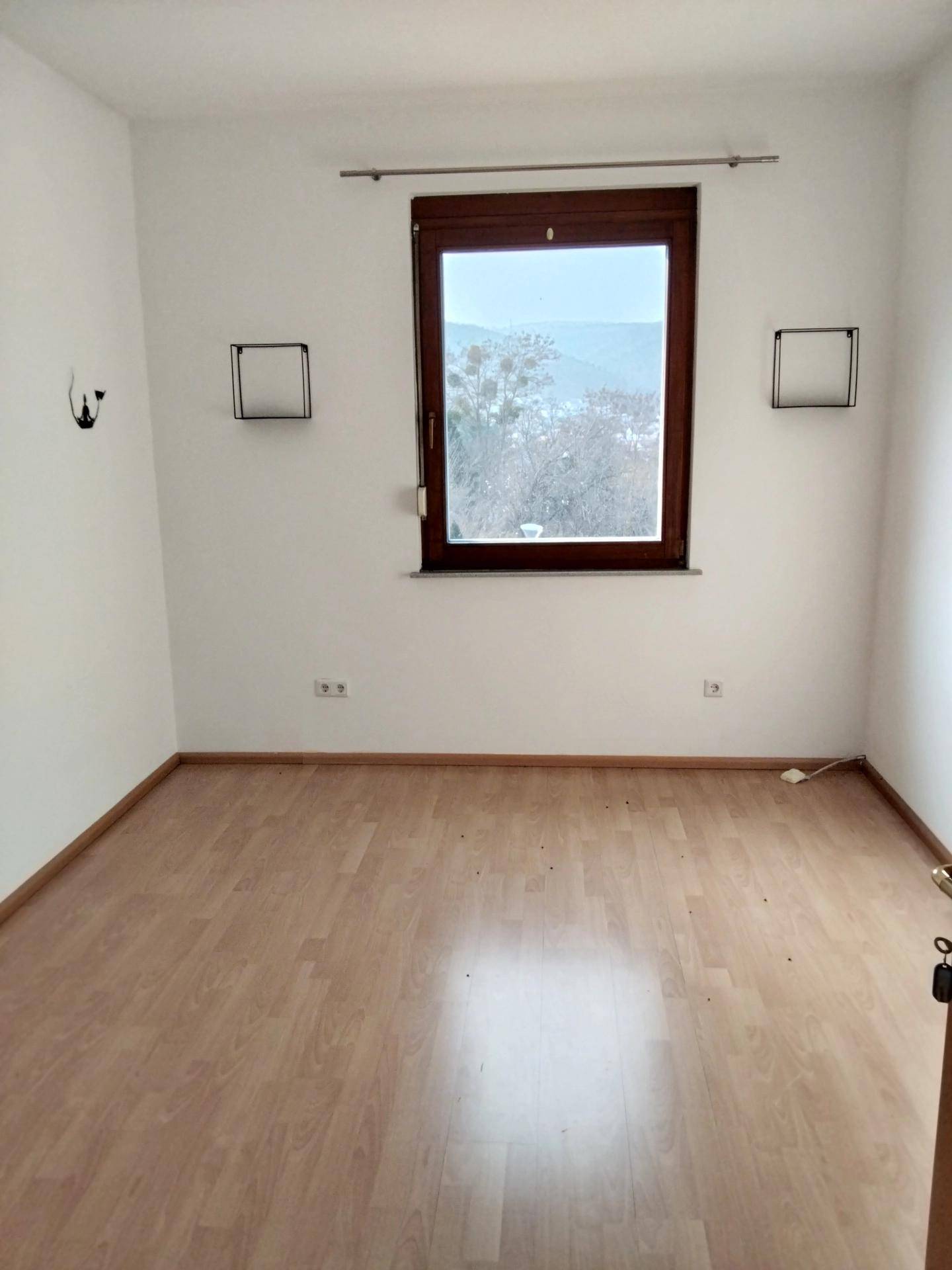 Leeres Schlafzimmer mit Laminatboden, weiß gestrichenen Wänden und Fenster.