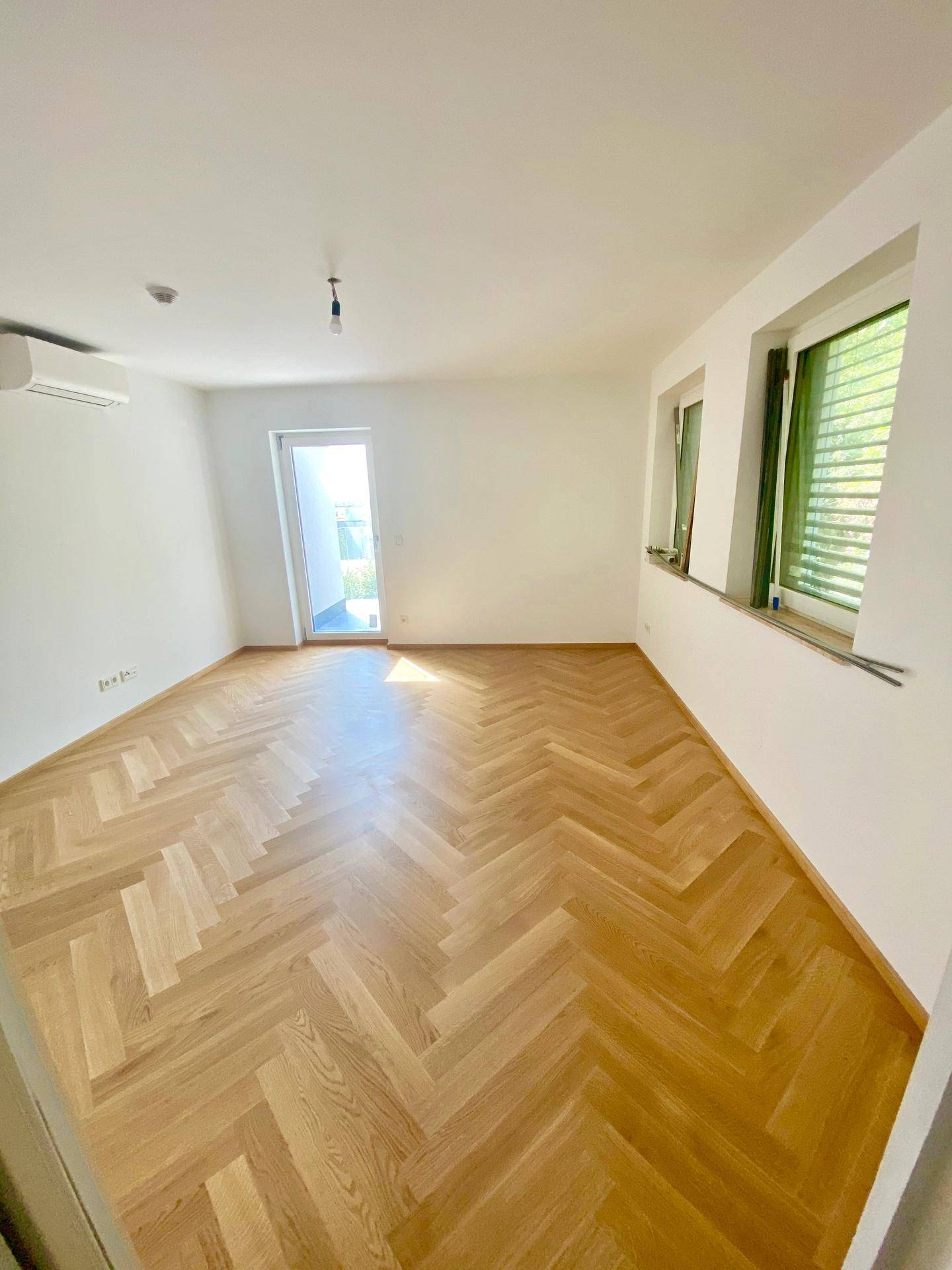 Helles Zimmer mit Fischgrätparkett und Zugang zu einem Außenbereich.
