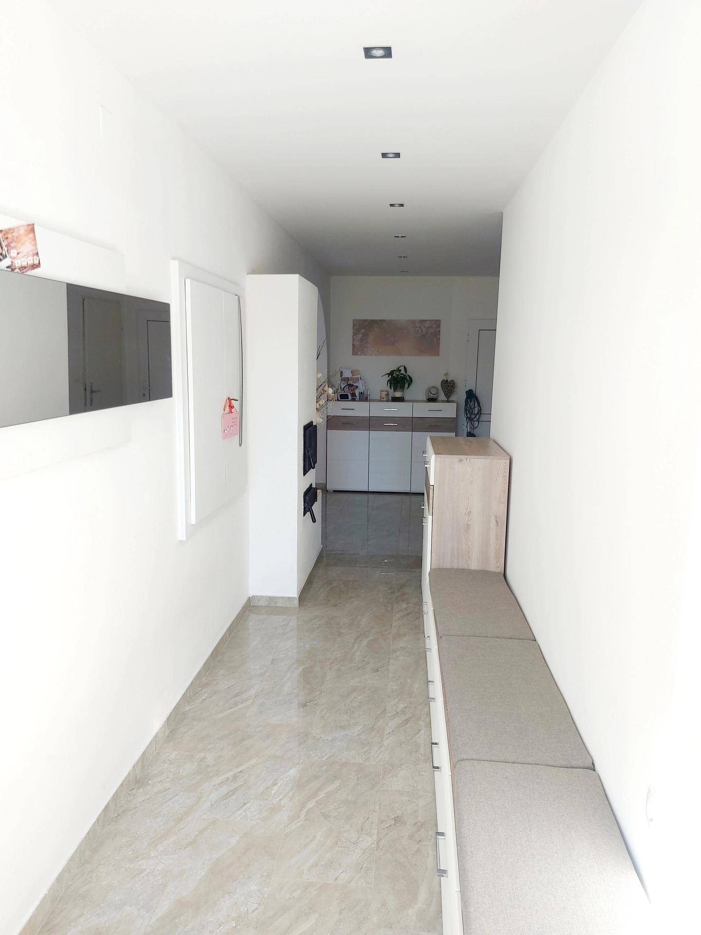 Langer, heller Flur mit Fliesenboden, Einbauschrank und einer Sitzbank.