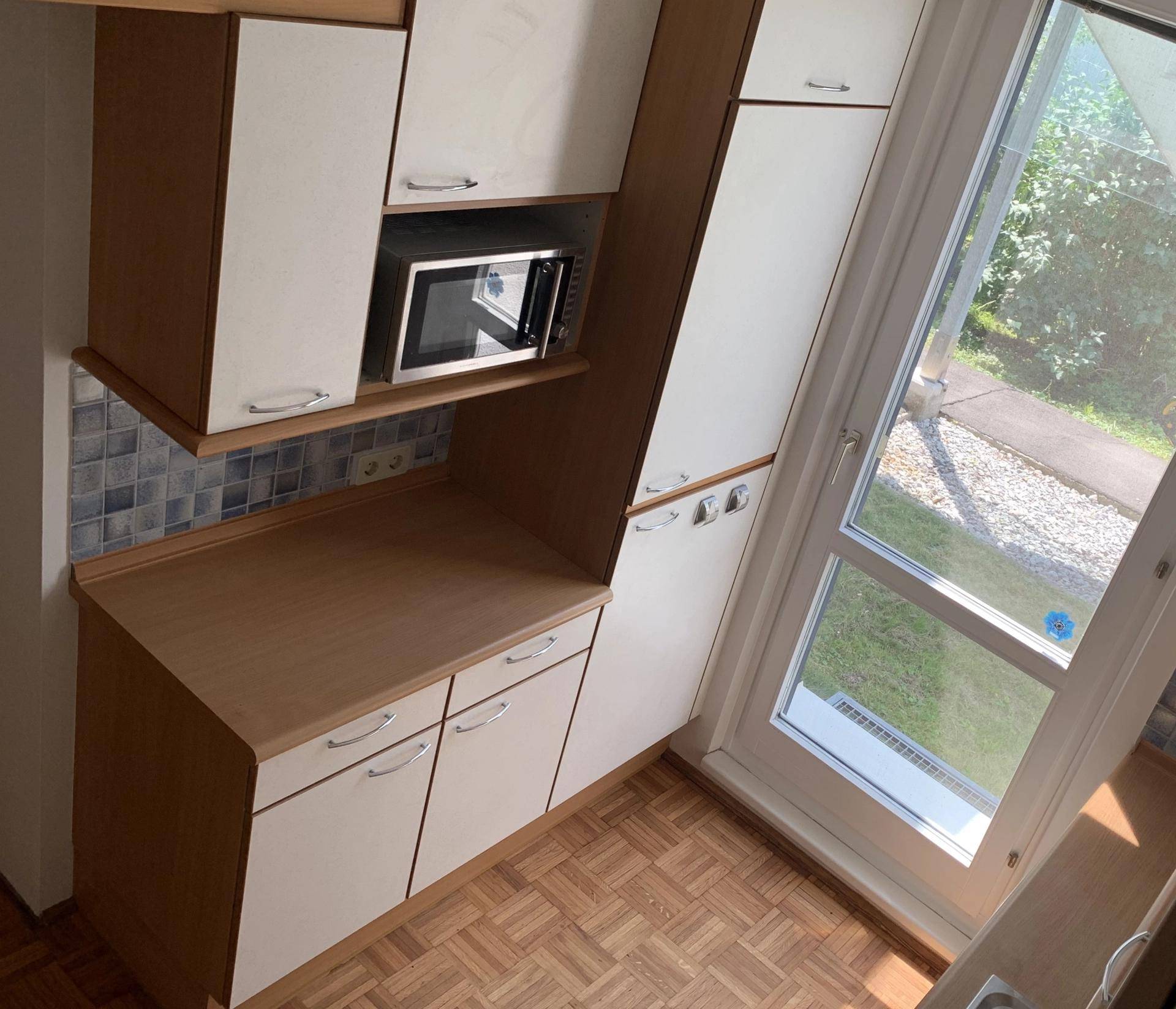 Küchenbereich mit integrierter Mikrowelle und einer Fenstertür, die Zugang zum Außenbereich bietet.