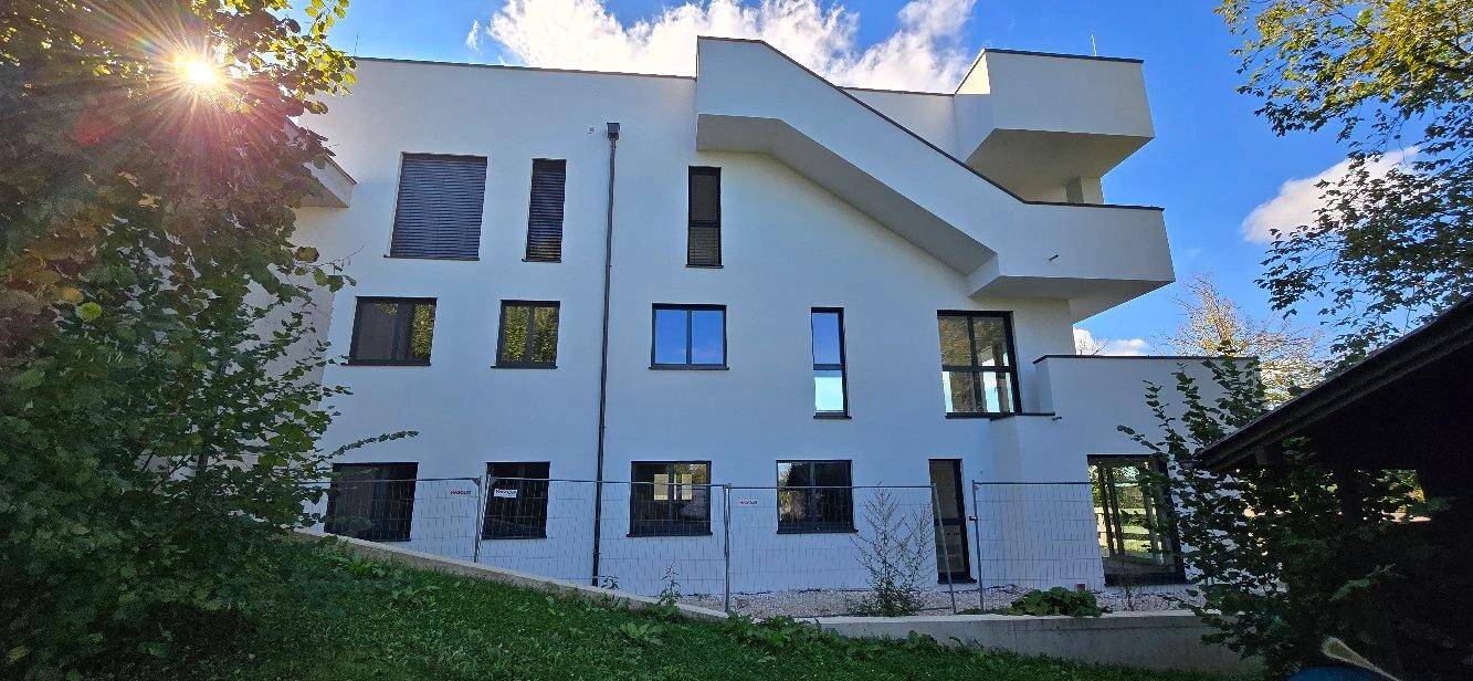 Moderne weiße Gebäudefassade mit großen Fenstern und klaren Linien, umgeben von Grünflächen.