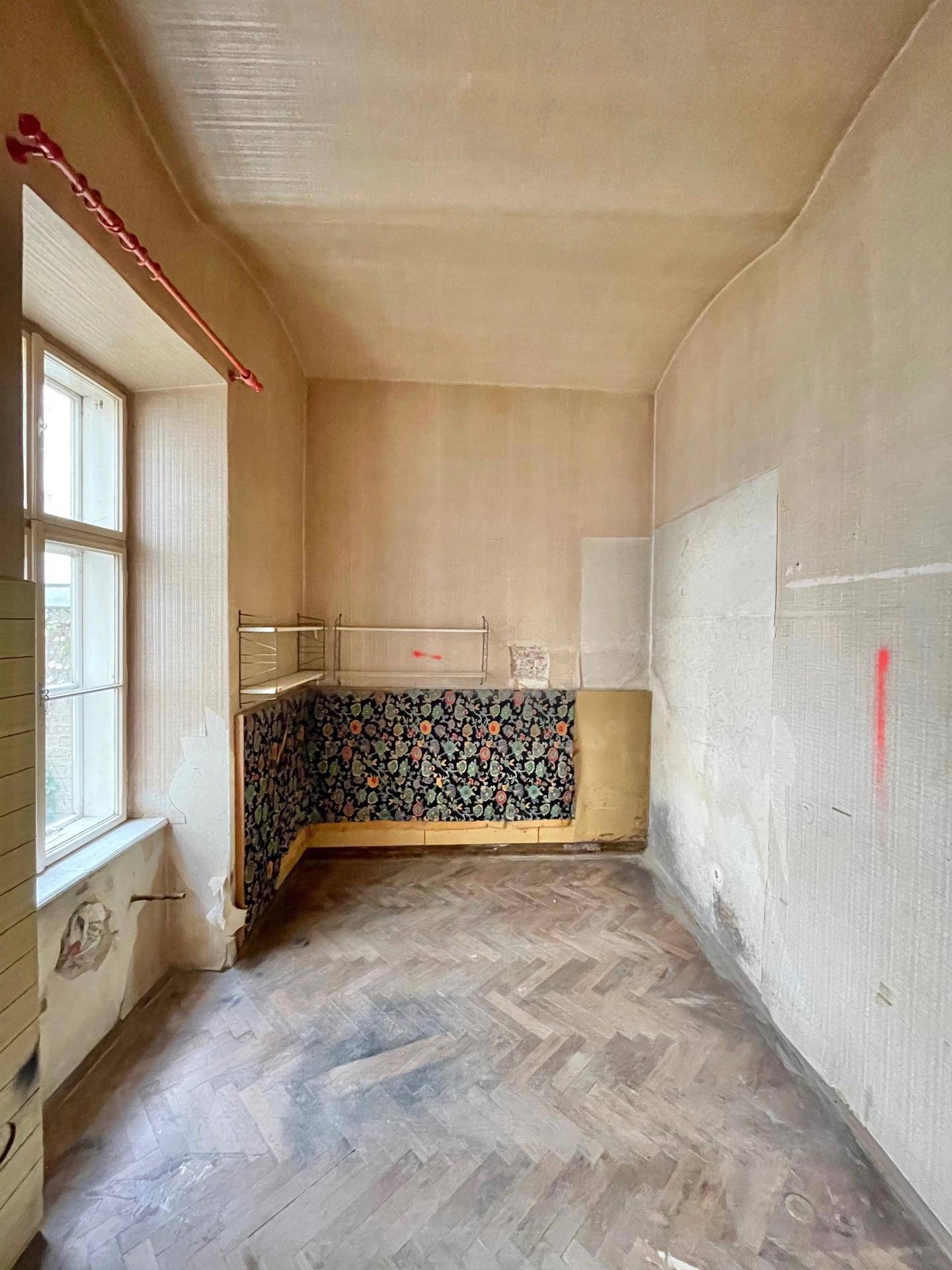 Kleiner Raum in sanierungsbedürftigem Zustand mit Fenster und einfacher Bodenfläche.