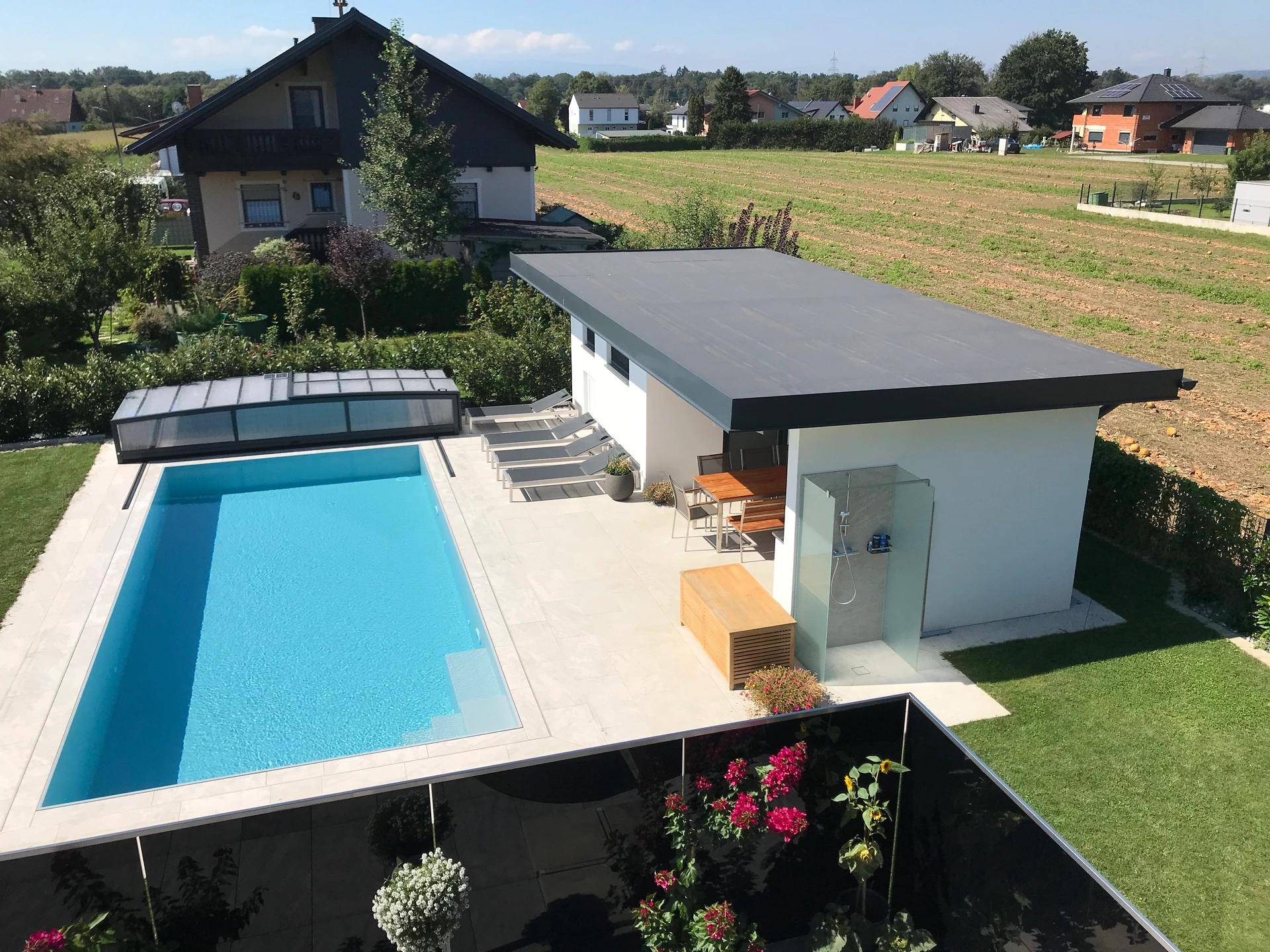 Panoramablick auf den Garten mit großem Pool, Poolhaus und weitem Blick über die Landschaft.