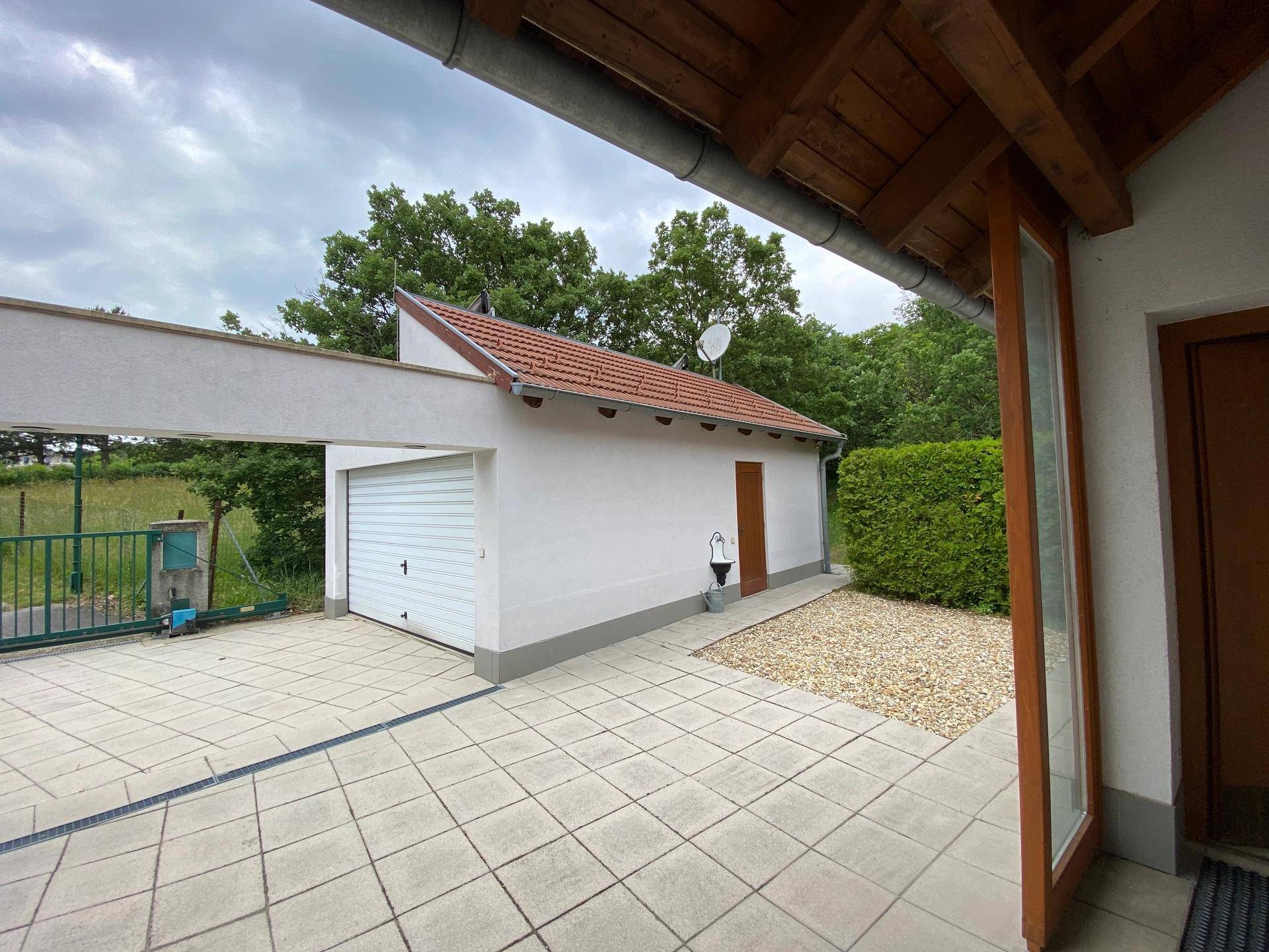 Garage mit gepflastertem Vorplatz und einem Carport, umgeben von Hecken.