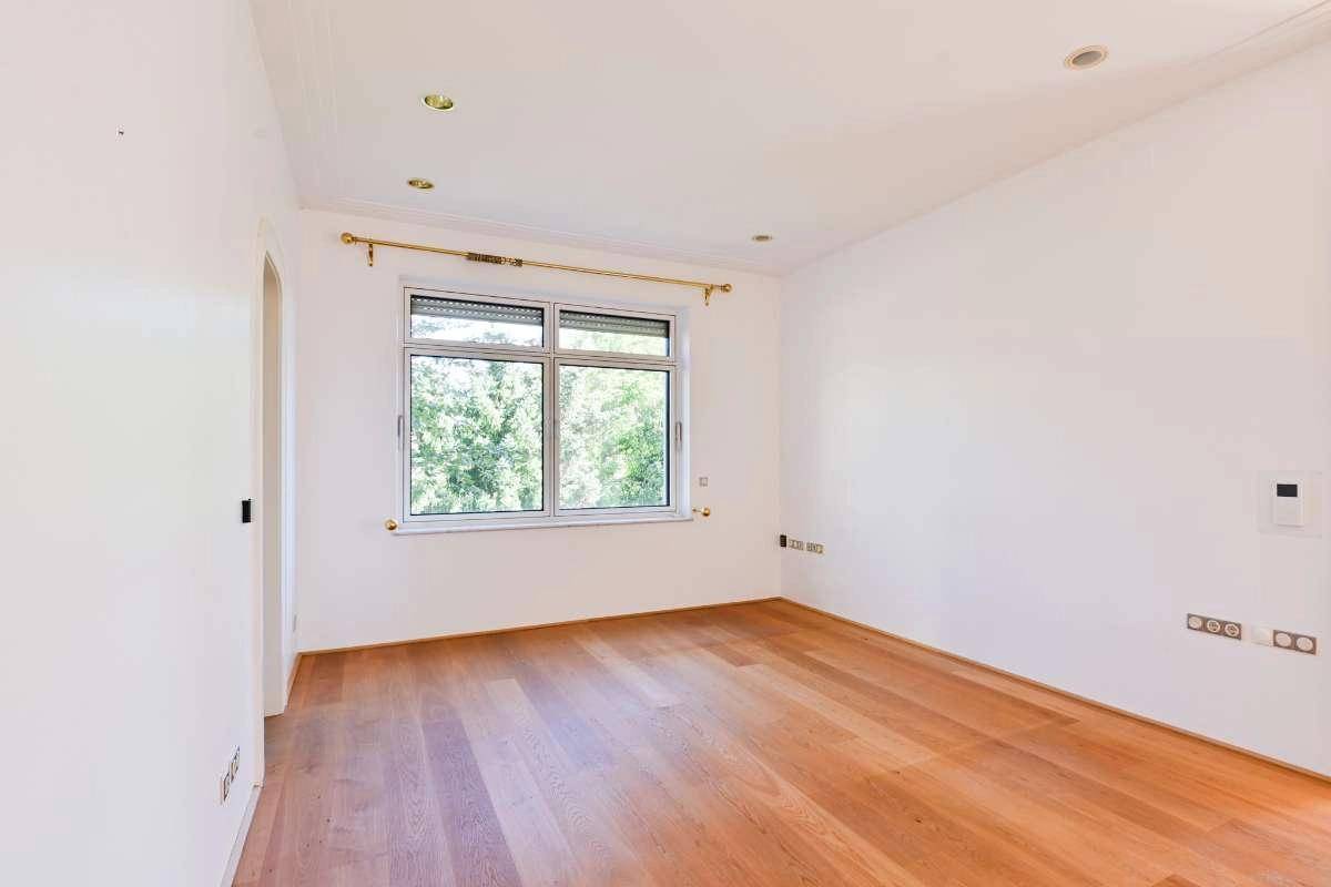 Geräumiges Zimmer mit Holzboden und breitem Fenster, das viel Tageslicht hereinlässt.