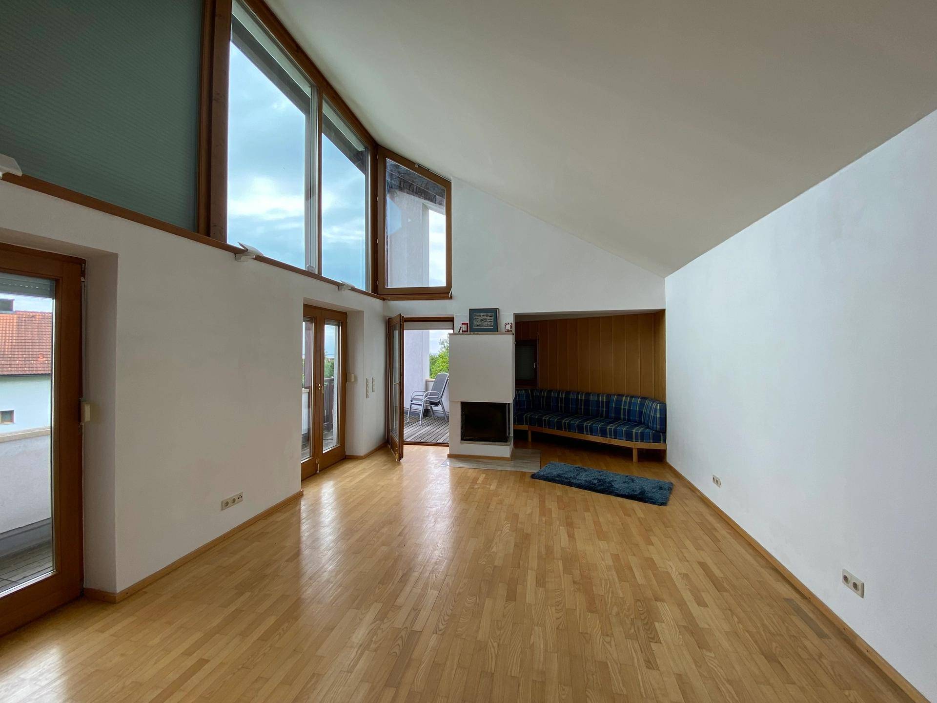 Helles Wohnzimmer mit Kamin, Holzboden und Zugang zu einem Balkon.