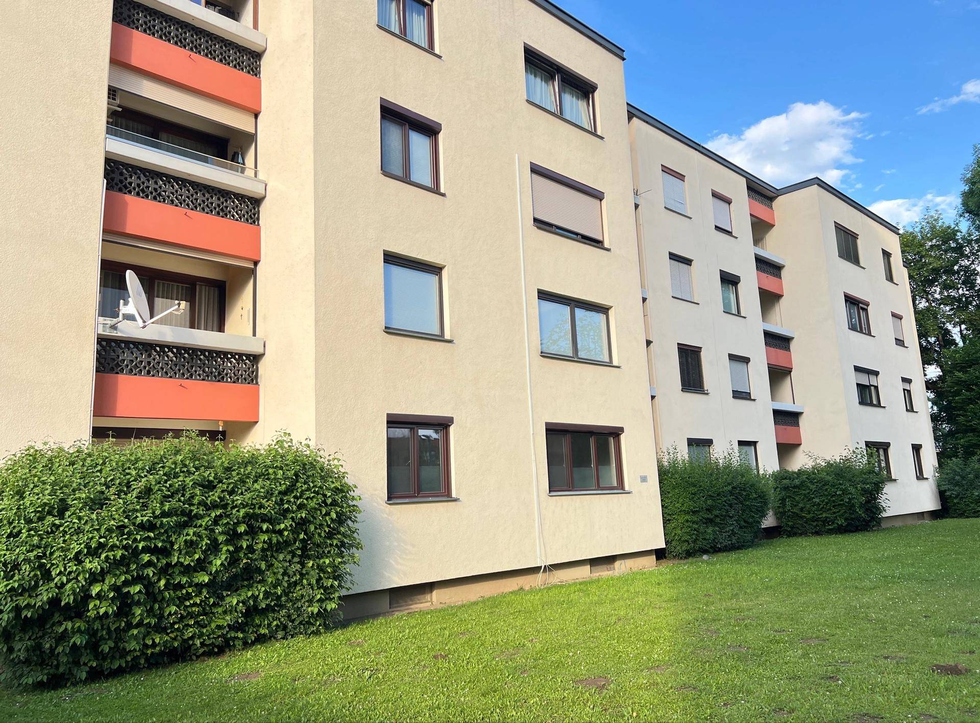 Mehrfamilienhaus mit mehreren Etagen, Balkonen und gepflegter Grünfläche.