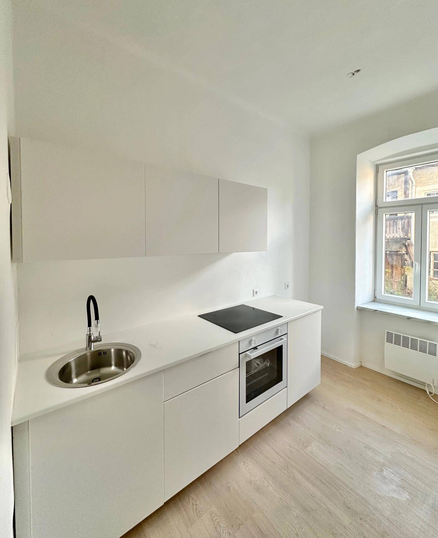 Moderne, helle Küche mit weißen Schränken, Spüle und Kochfeld.
