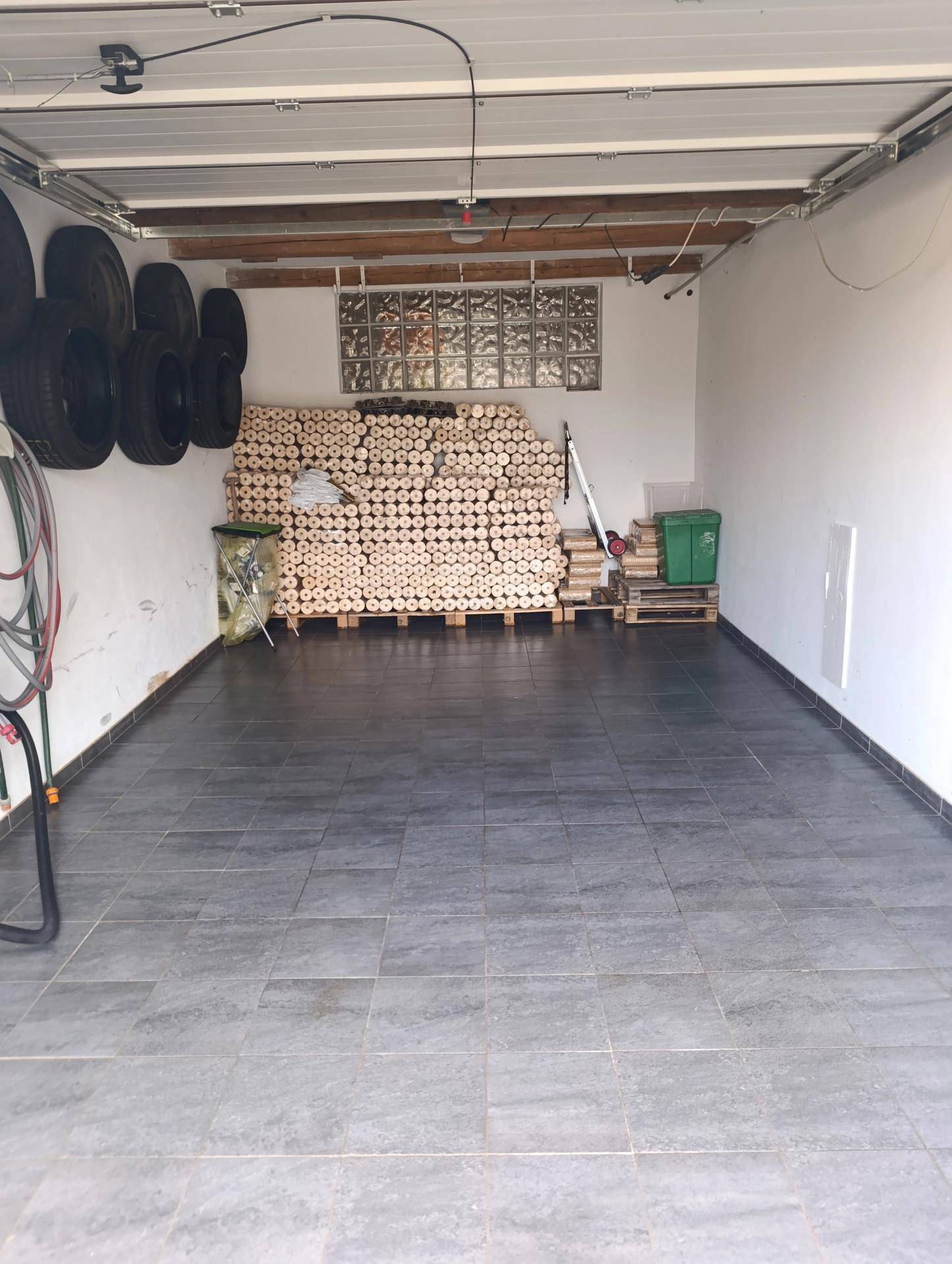 Geräumige Garage mit Fliesenboden und gestapeltem Brennholz an der Wand.
