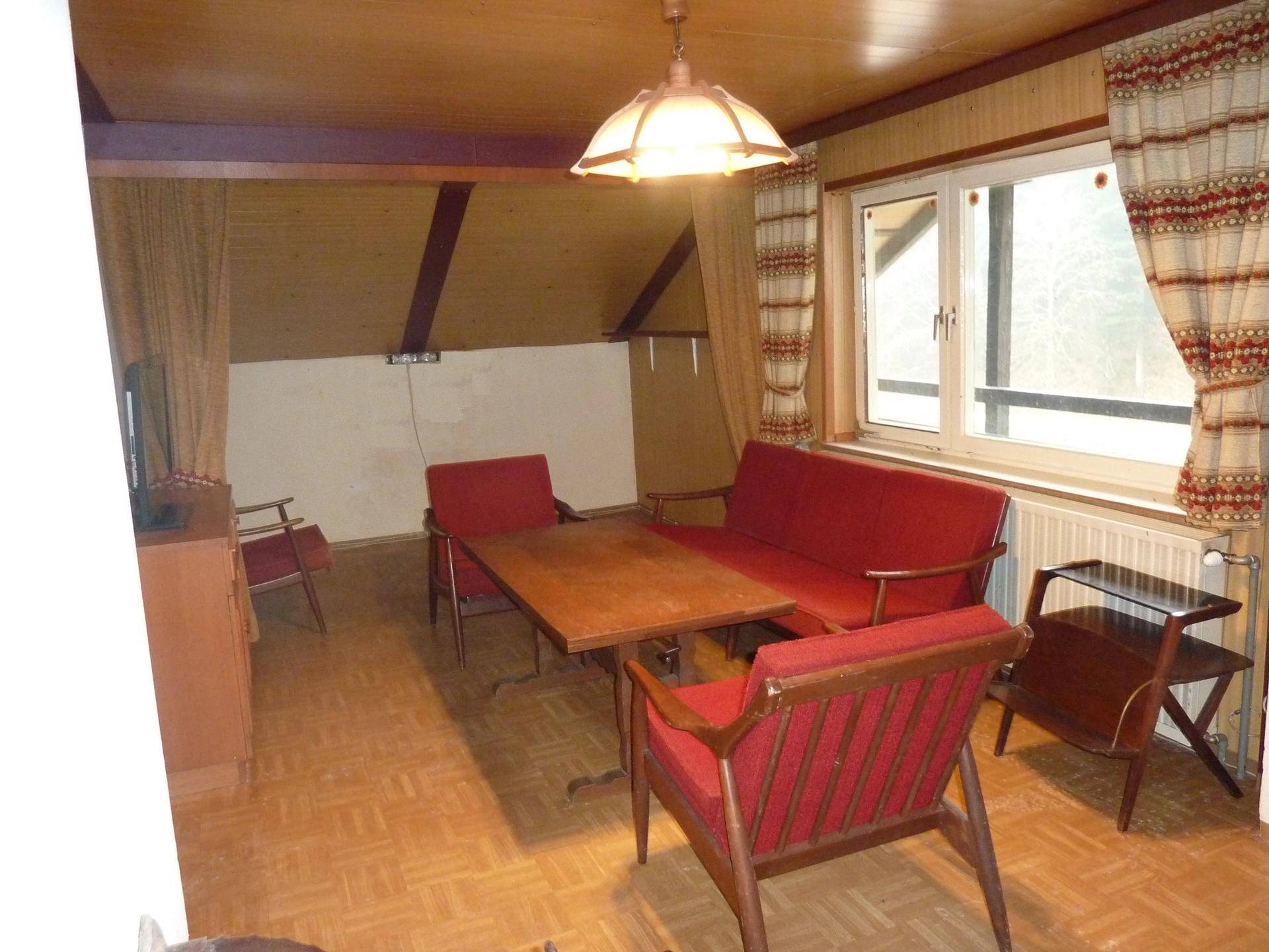 Wohnzimmer im Dachgeschoss mit Holzbalken, roten Möbeln und Blick ins Grüne.