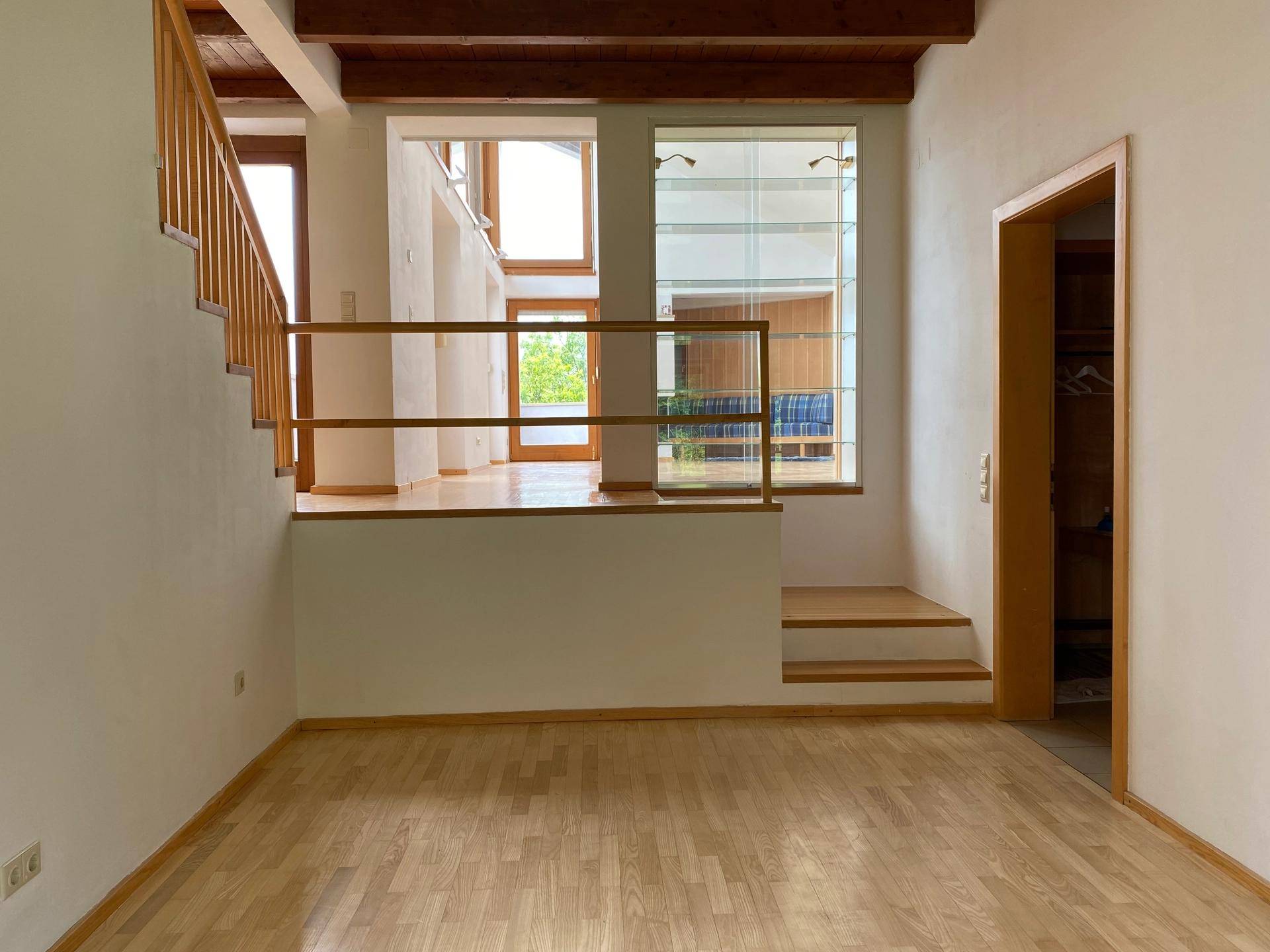 Heller Flurbereich mit Holztreppe, Holzboden und Blick auf große Fenster.