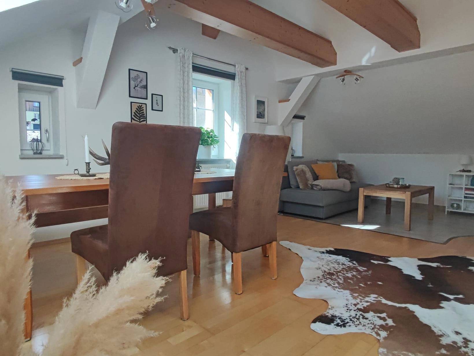 Geräumiger Wohn-Essbereich mit sichtbaren Holzbalken, Dachschrägen und rustikalen Möbeln.
