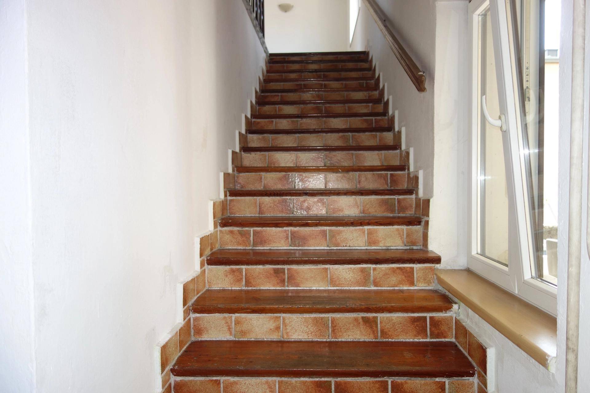 Geflieste Treppe mit Holzstufen und einem Fenster, das nach oben führt.