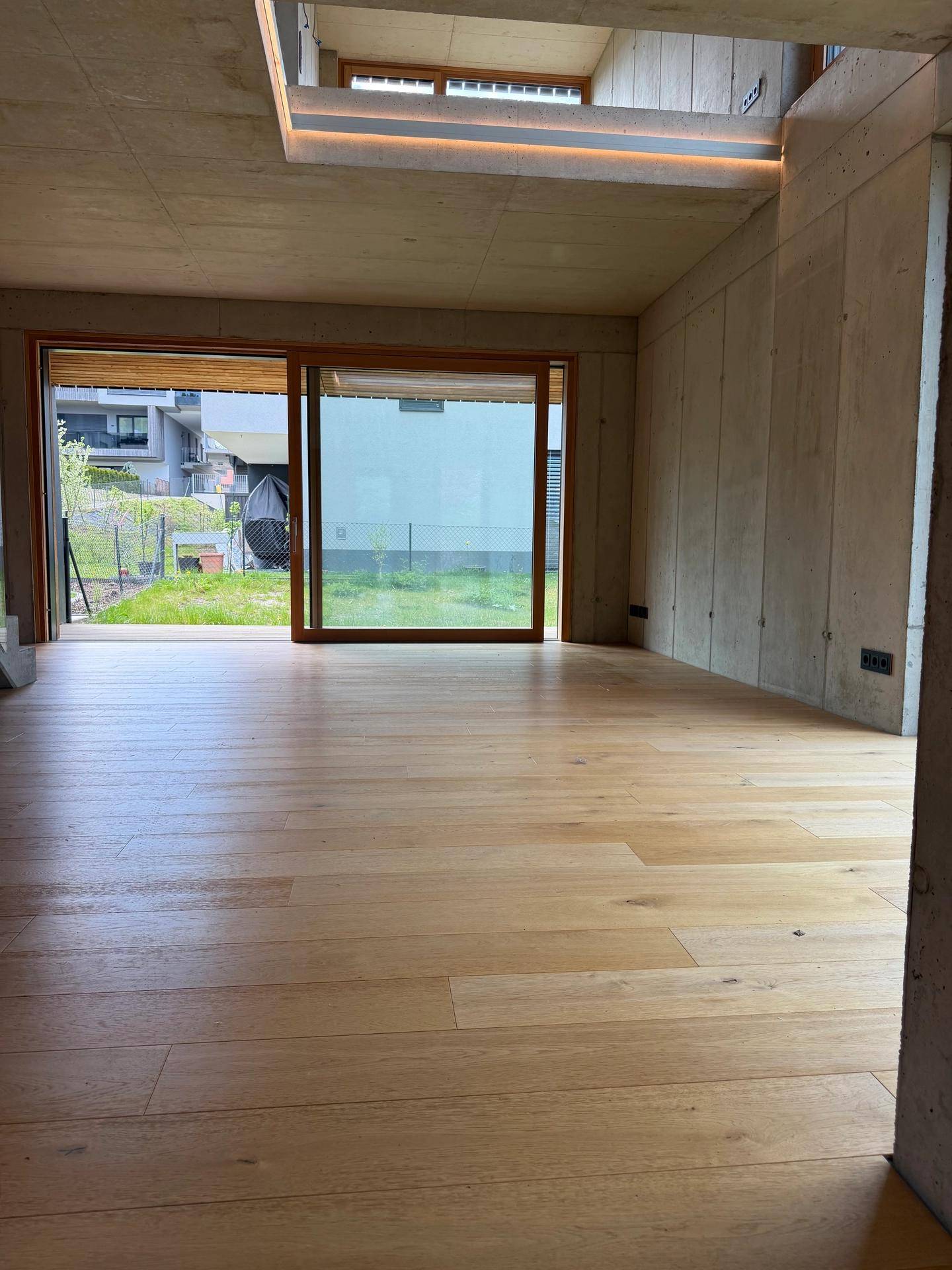 Lichtdurchfluteter Raum mit Holzboden, Sichtbetondecke und großen Schiebetüren zum Garten.