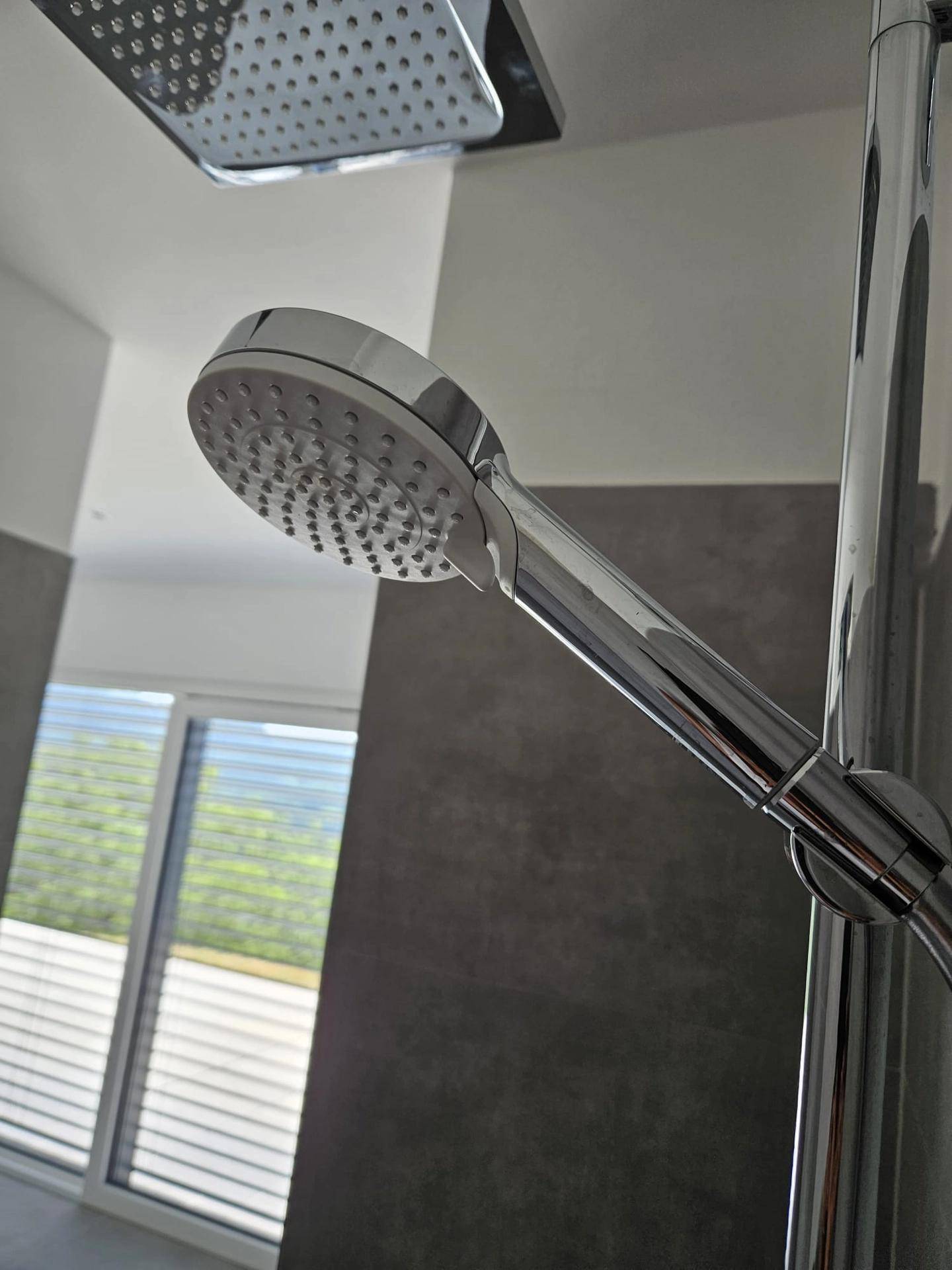 Detailaufnahme eines modernen Regenduschkopfs in einem Badezimmer mit grauen Fliesen.