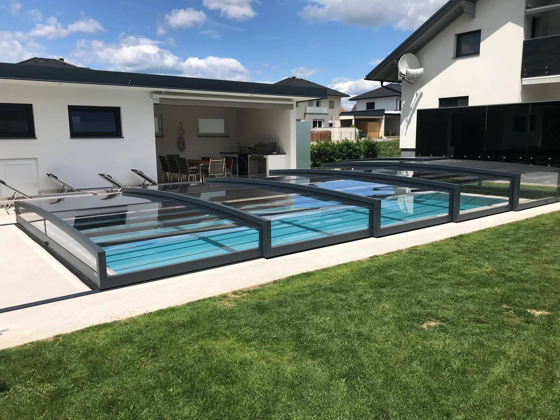 Weitläufiger Poolbereich mit verschiebbarer Abdeckung und Blick auf das moderne Wohnhaus.