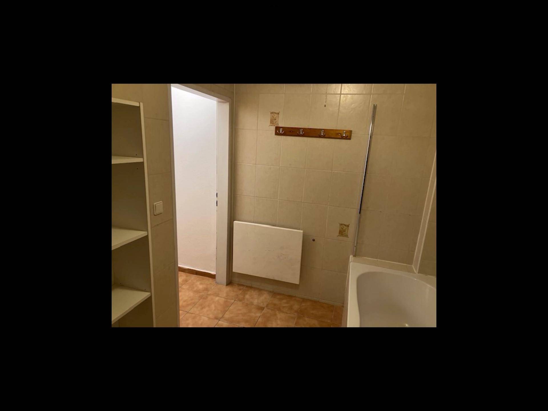 Badezimmer mit hellbraunen Fliesen, Badewanne und Heizkörper, das Renovierungsbedarf aufweist.