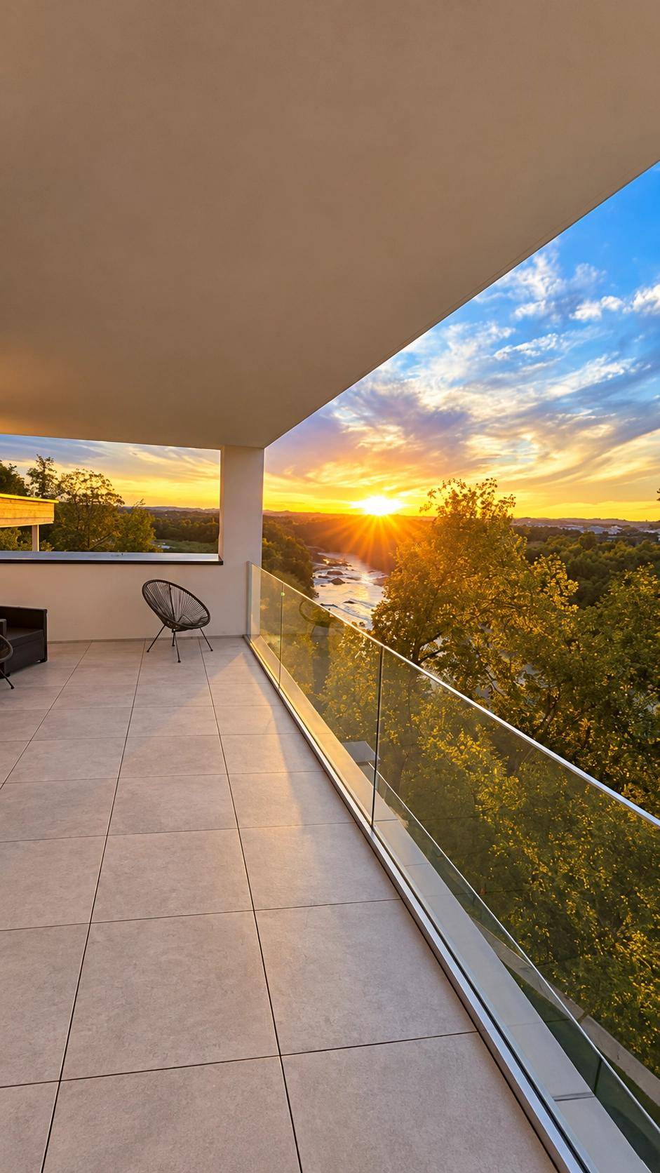 Geräumiger Balkon mit Glasgeländer und atemberaubendem Sonnenuntergangsblick über den Fluss.