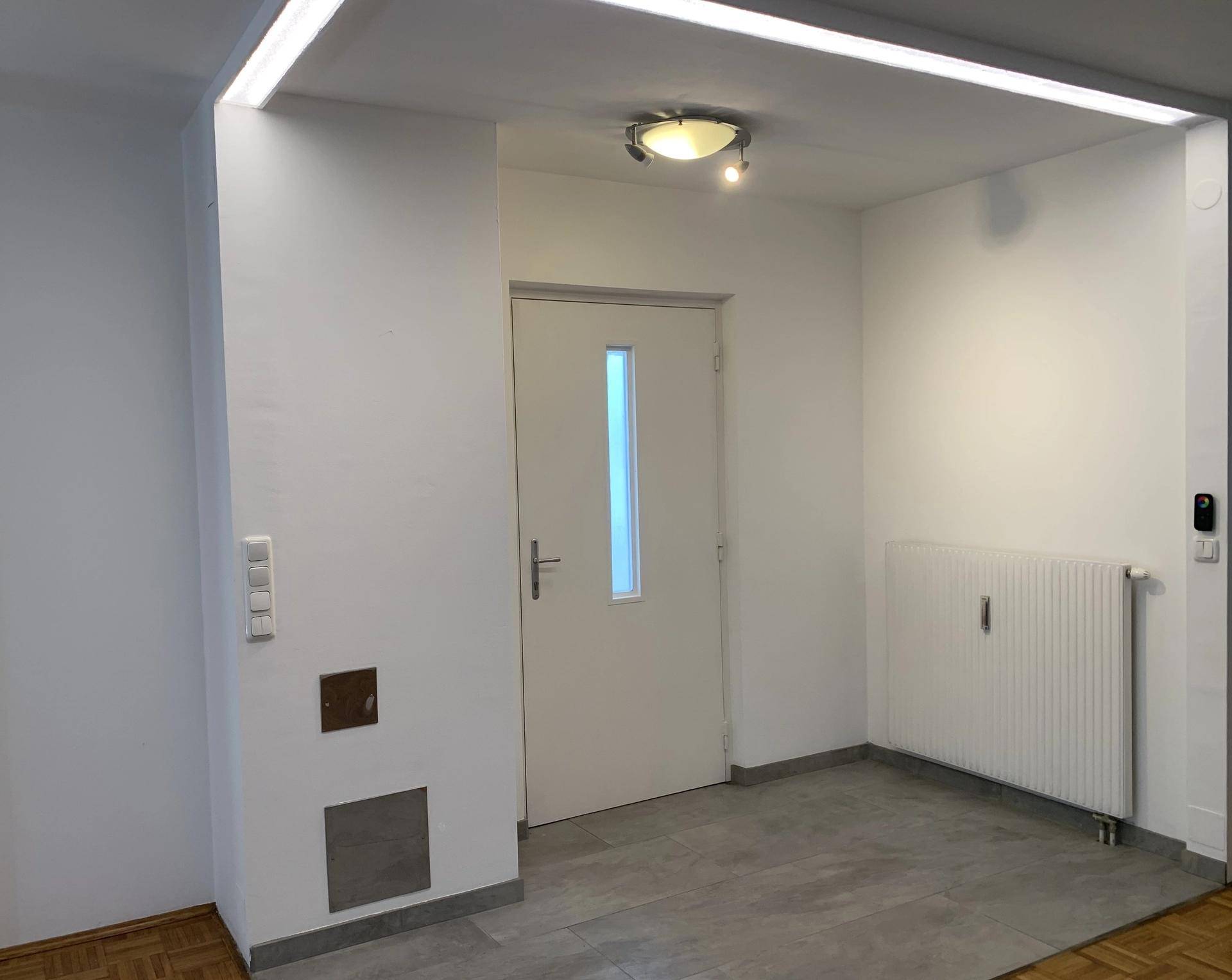 Heller Eingangsbereich mit weißer Tür, Heizkörper und modernen Deckenleuchten.
