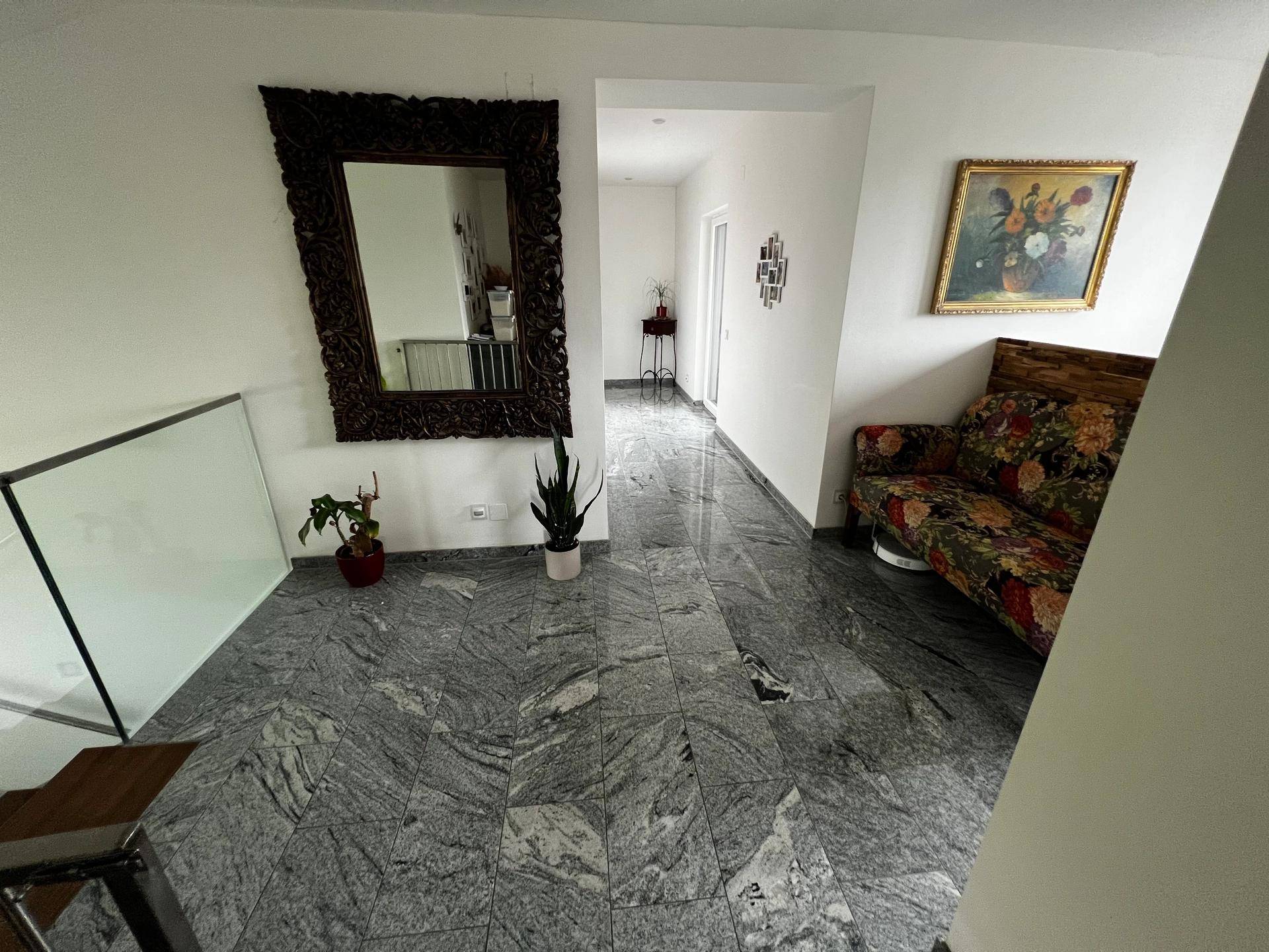 Geräumiger Flur mit grauem Fliesenboden, großem Spiegel und floralem Sofa.