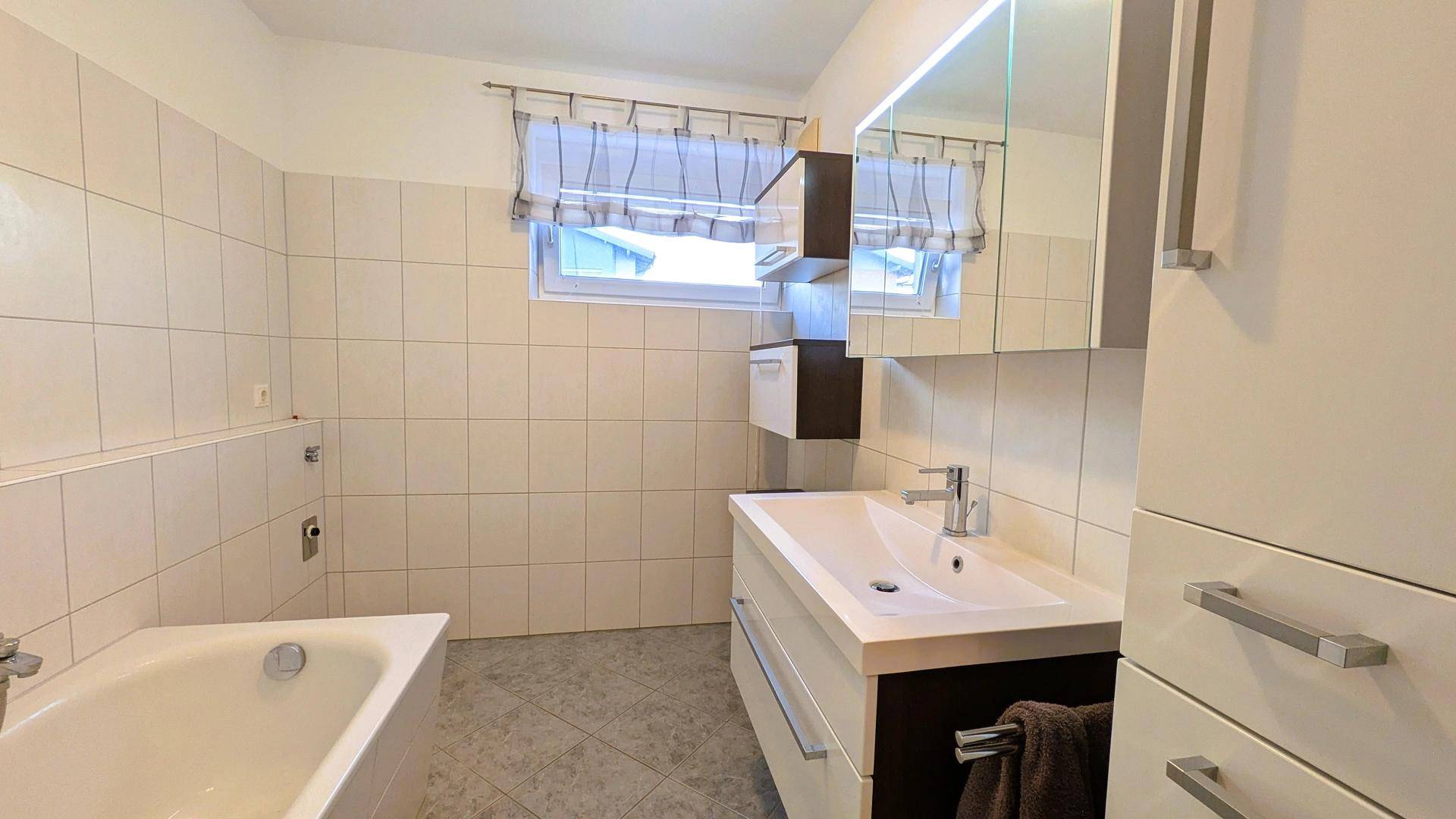 Badezimmer mit Badewanne, Waschtisch und Spiegelschrank, hell gefliest und funktional.