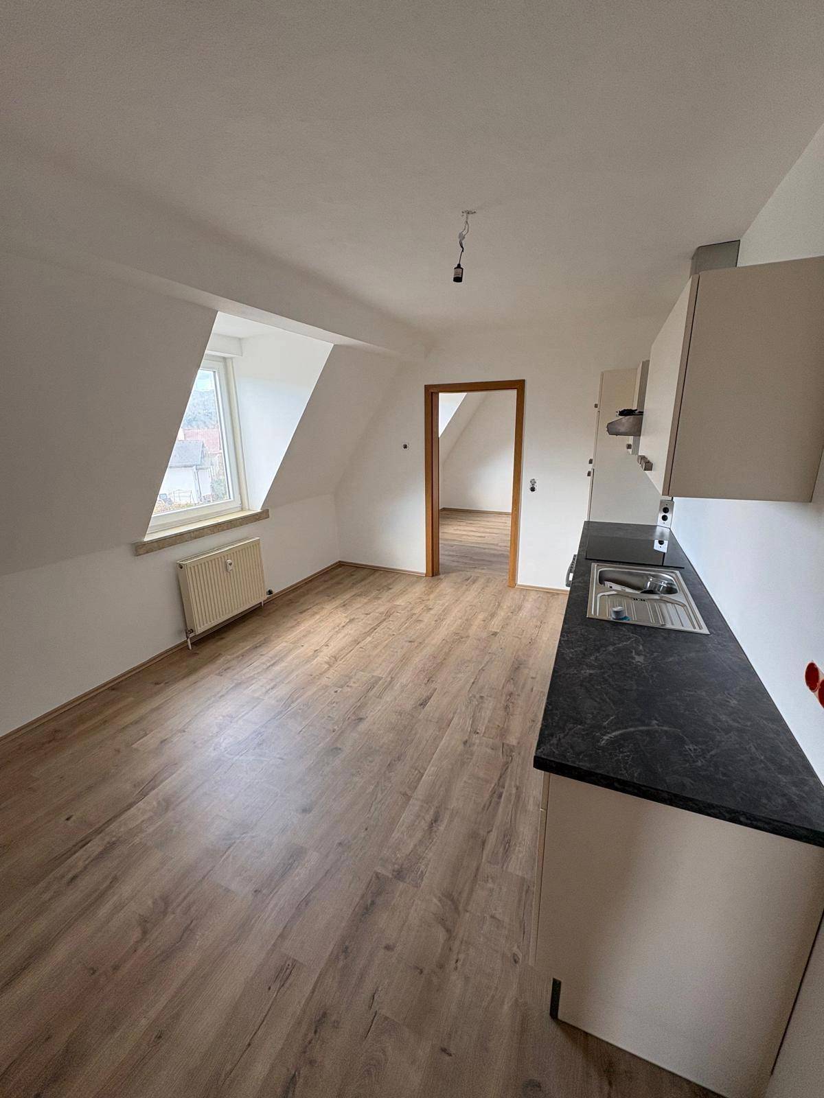 Teilweise eingerichtete Küche mit Spüle, Laminatboden und Dachschräge in einem hellen Raum.