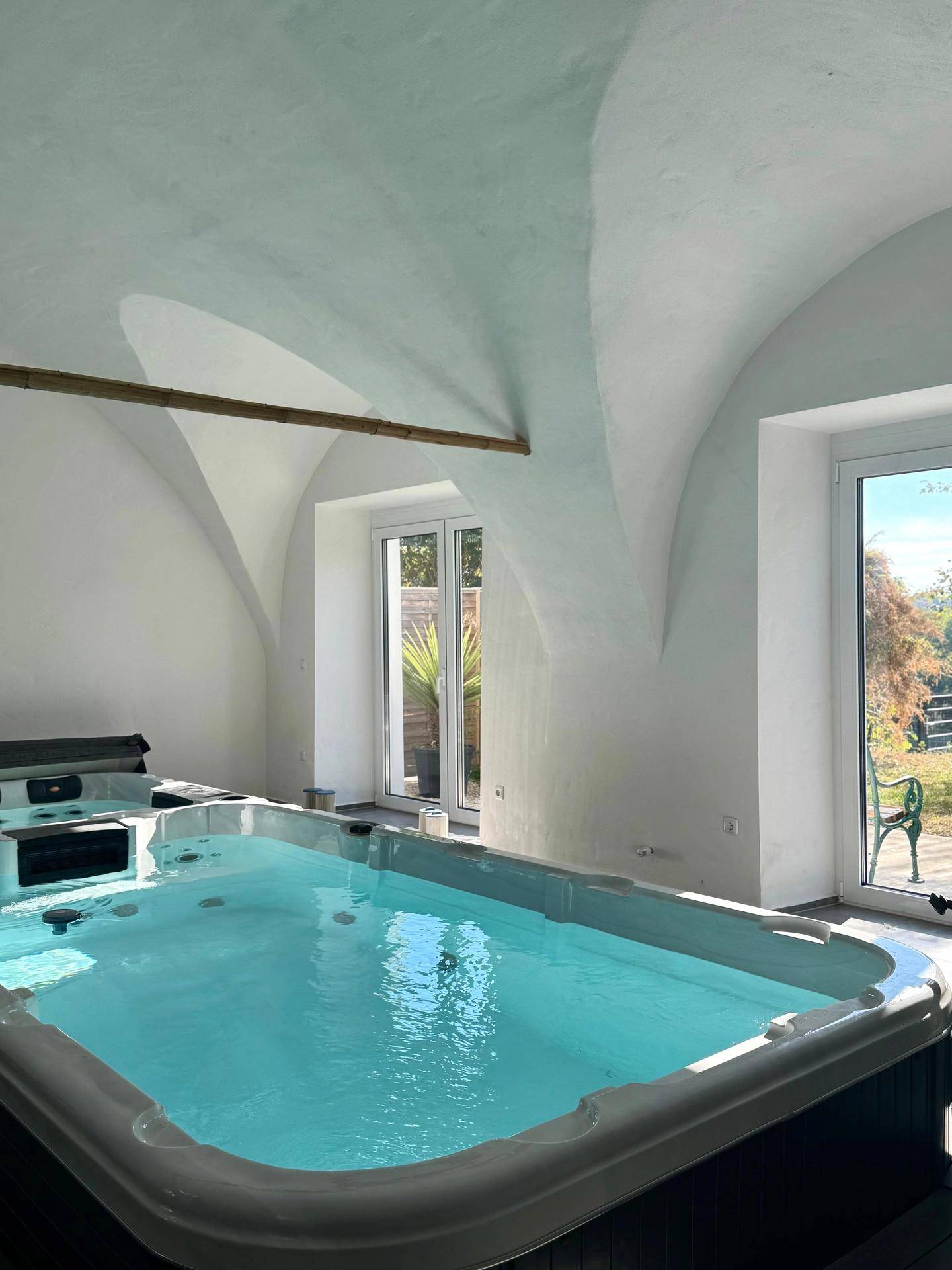 Heller Raum mit modernem Swim-Spa und Whirlpool, umgeben von großen Fenstern und Gewölbedecken.