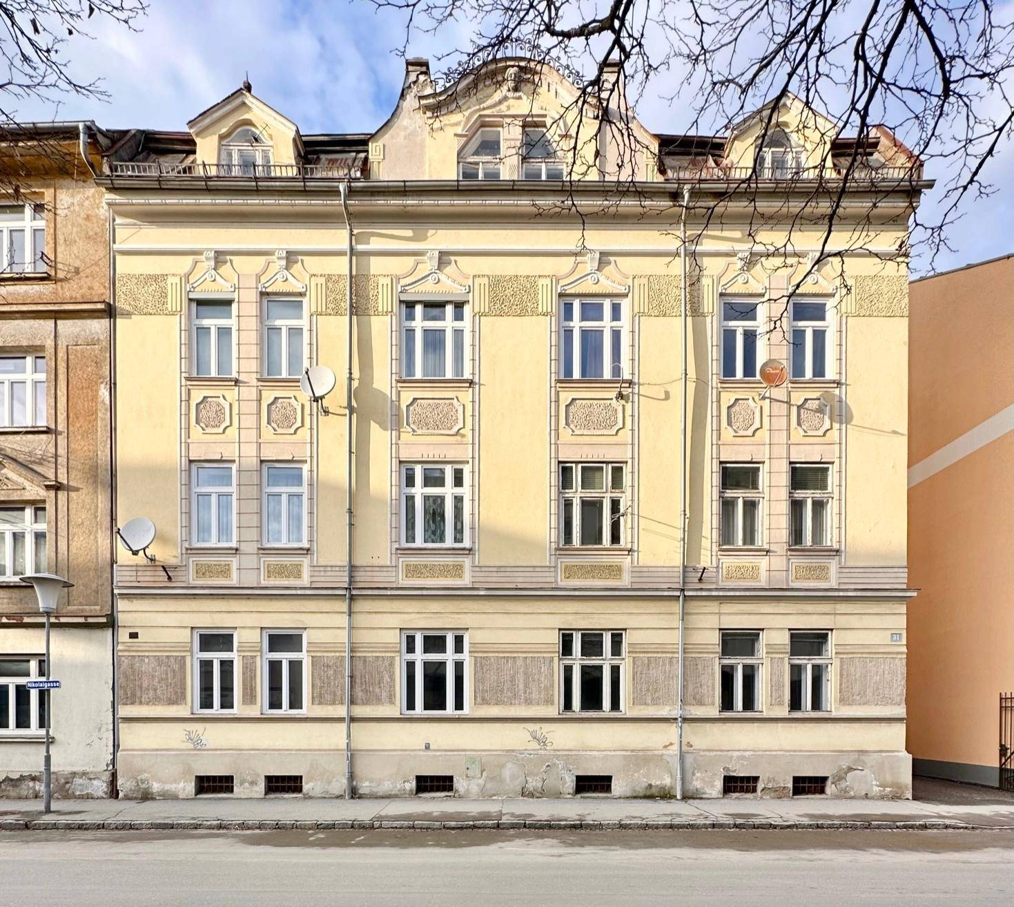 Vorderansicht eines historischen Gebäudes mit gelber Fassade und dekorativen Elementen.