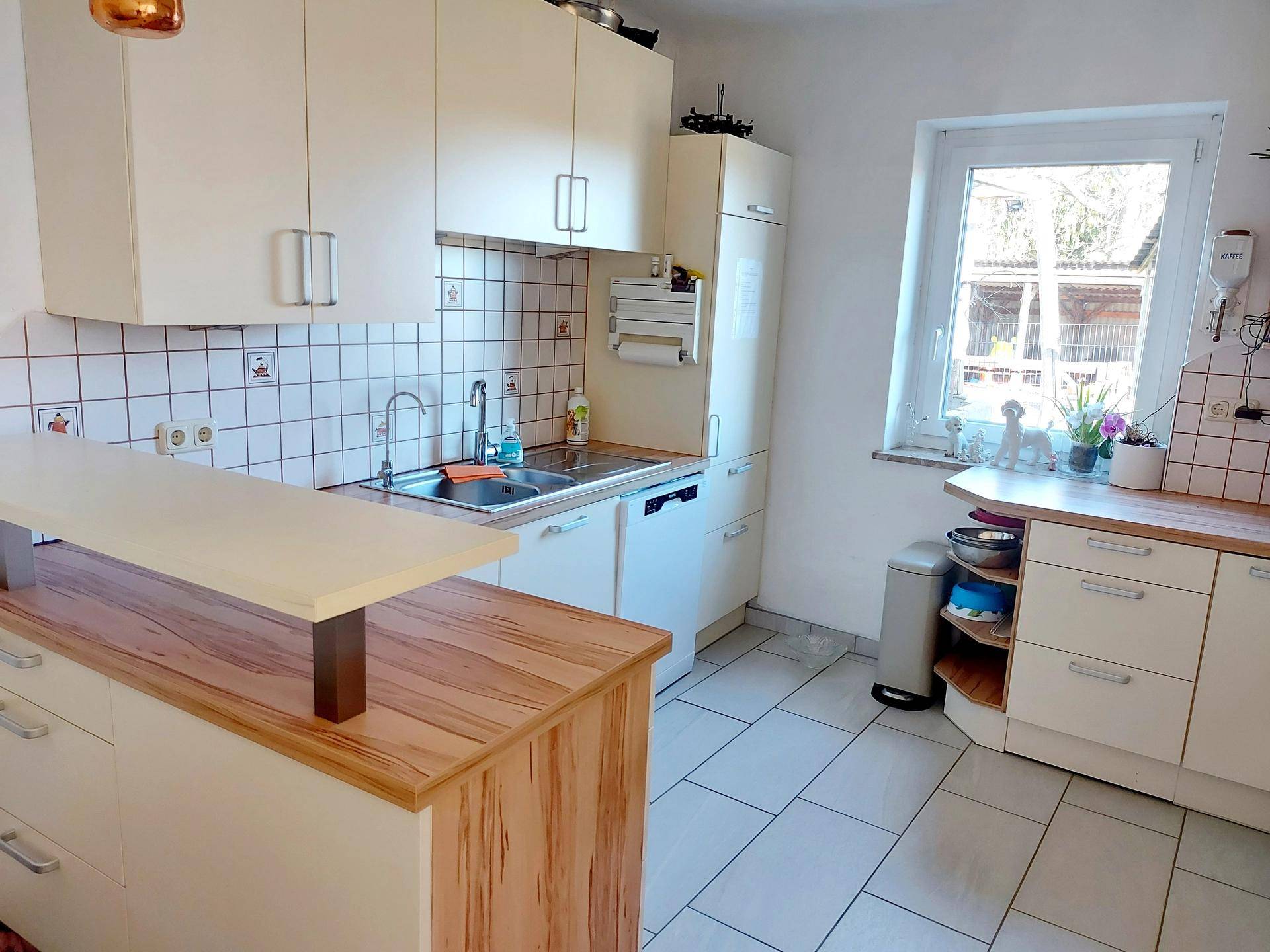 Funktionale Küche mit hellen Schränken, Holztheke und einem Fenster mit Blick nach draußen.