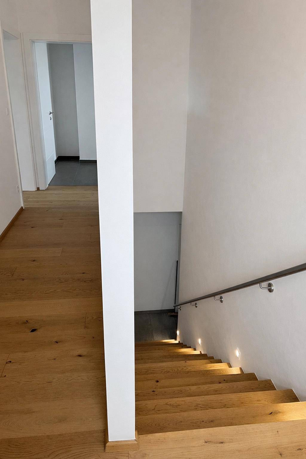 Heller Flur mit Holztreppe und indirekter Beleuchtung, die zu den oberen Etagen führt.