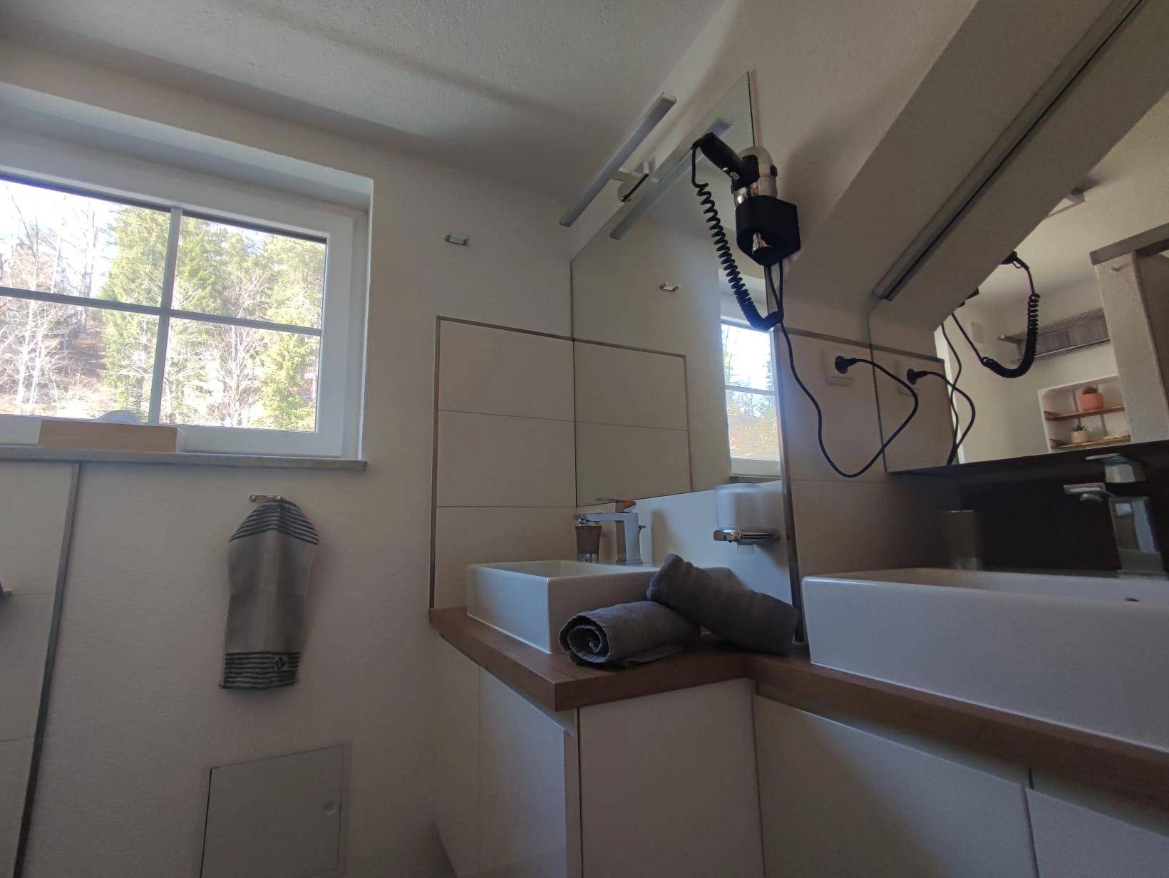 Modernes Badezimmer mit Doppelwaschbecken, großem Spiegel und Fenster mit Waldblick.