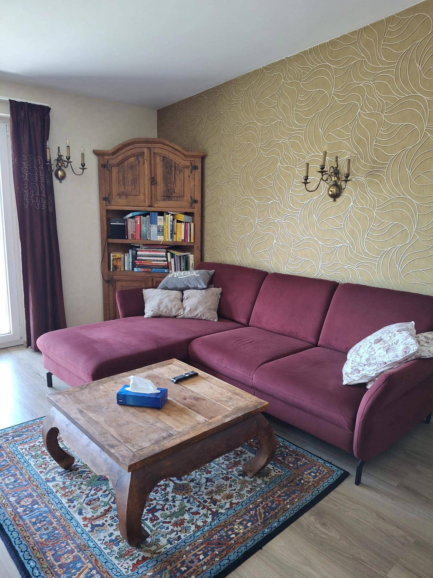 Gemütliches Wohnzimmer mit großem lila Sofa, Holztisch und einem traditionellen Teppich.