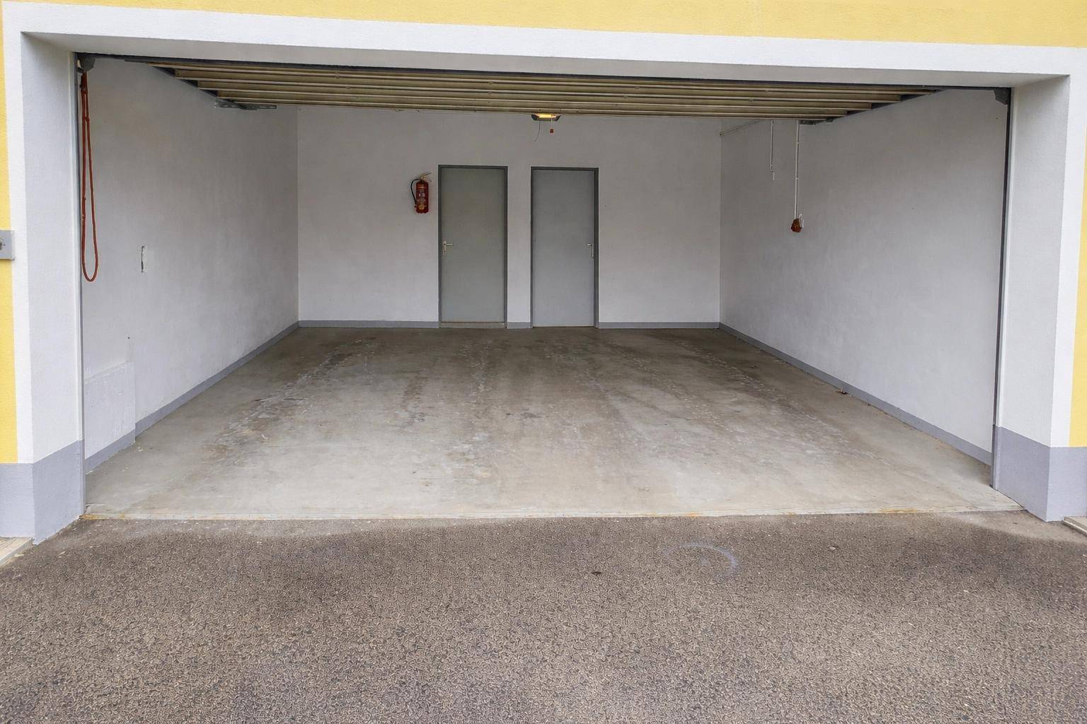 Leere Garage mit Betonboden, weißen Wänden und zwei Türen im hinteren Bereich.