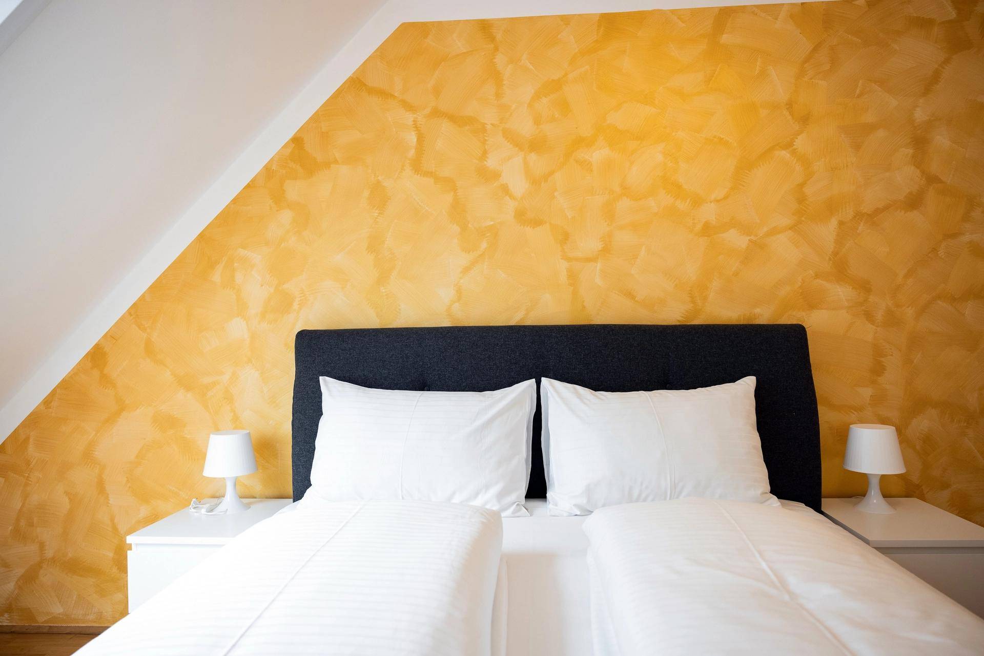 Nahaufnahme eines Doppelbettes mit weißen Kissen und einer gelb strukturierten Wand.