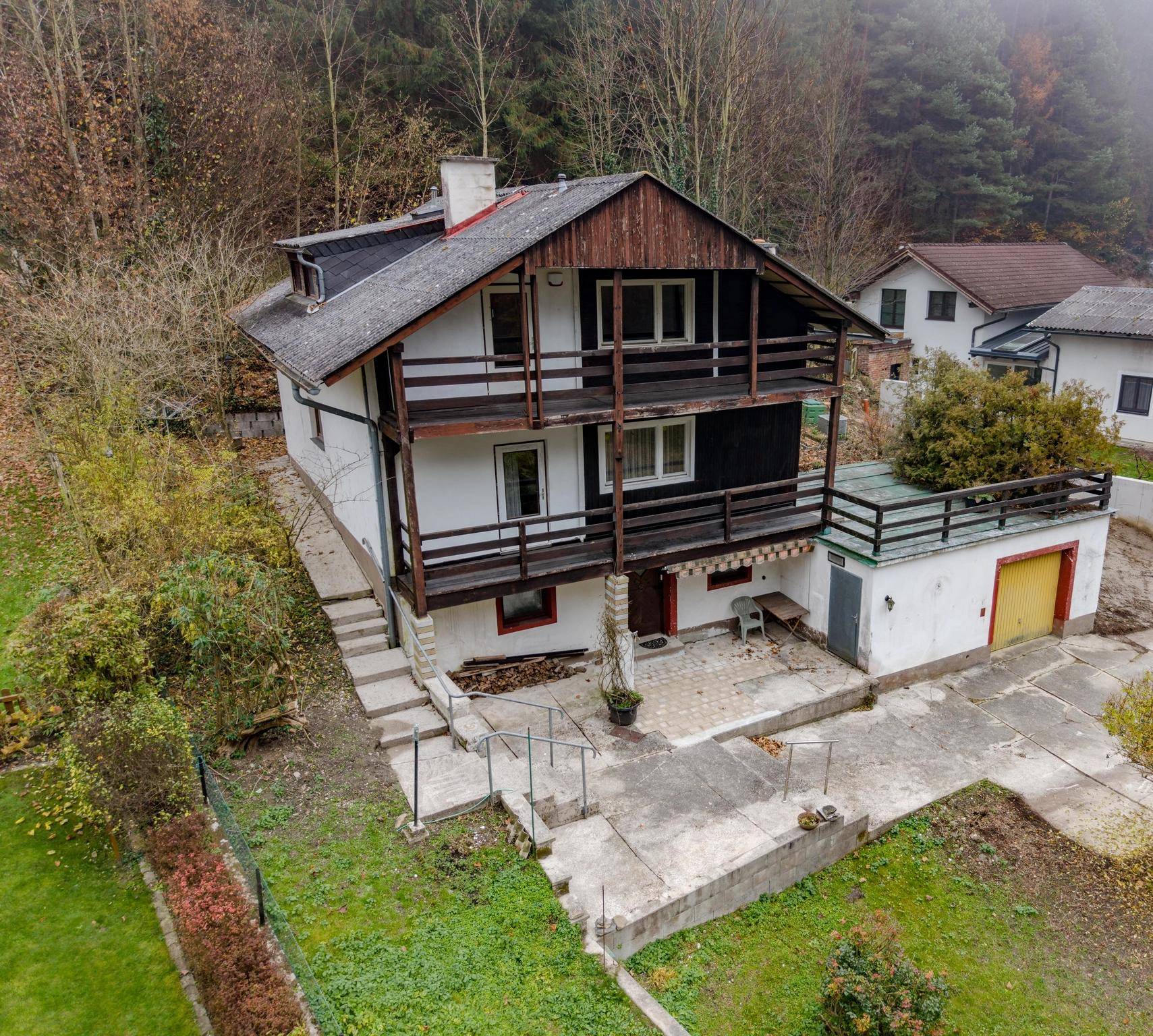 Freistehendes Haus mit Balkonen, Garage und umgebender Natur in nebliger Landschaft.