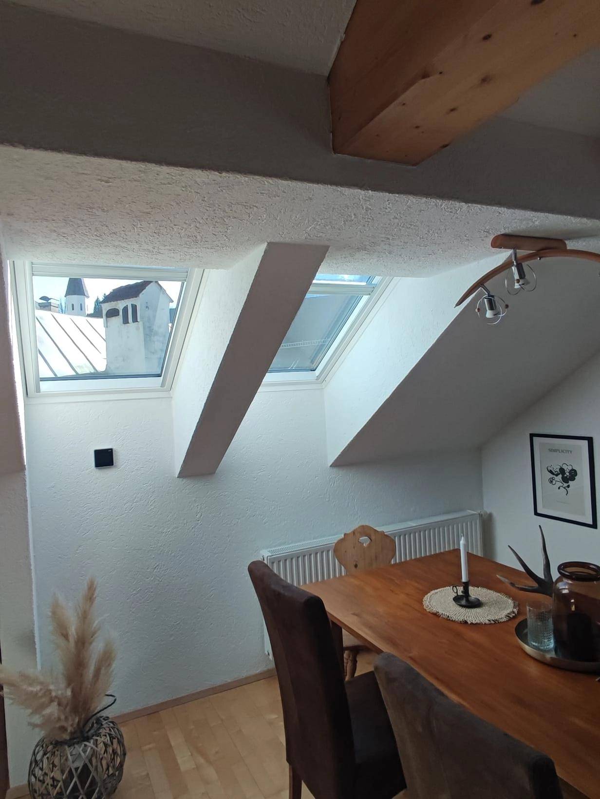 Heller Essbereich mit Holztisch, Dachfenstern und Blick auf einen Kirchturm.