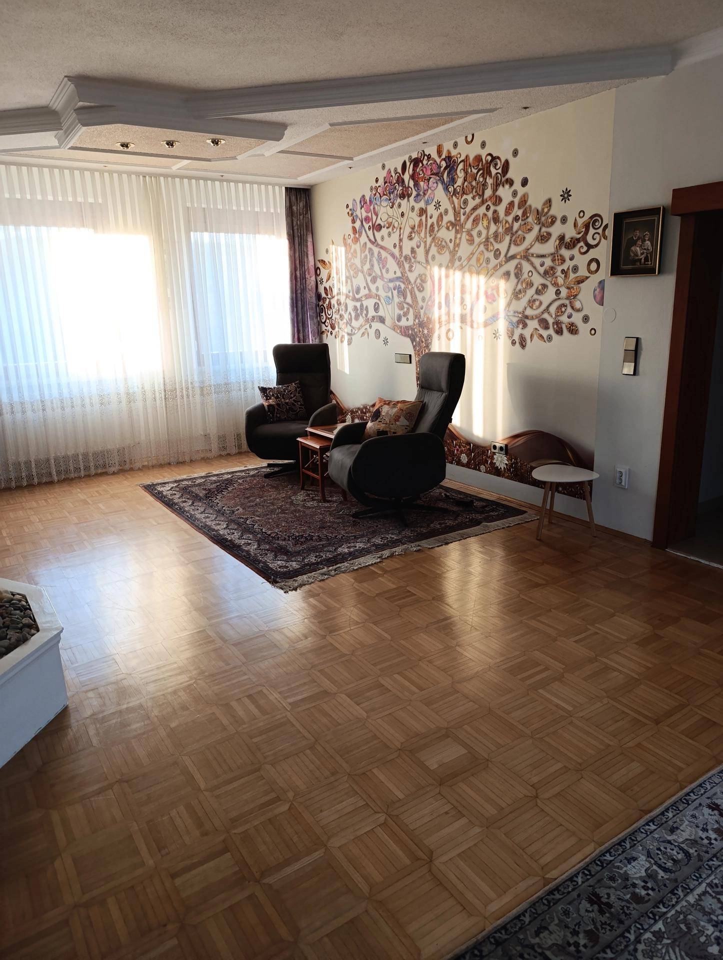 Helles Wohnzimmer mit Parkettboden, dekorativer Wandmalerei und bequemen Sesseln.