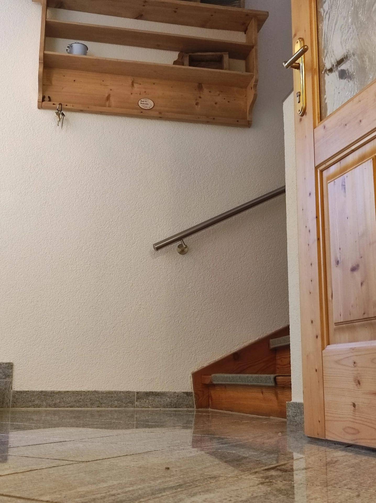 Eingangsbereich mit Holztreppe, gefliestem Boden und einer rustikalen Holztür.