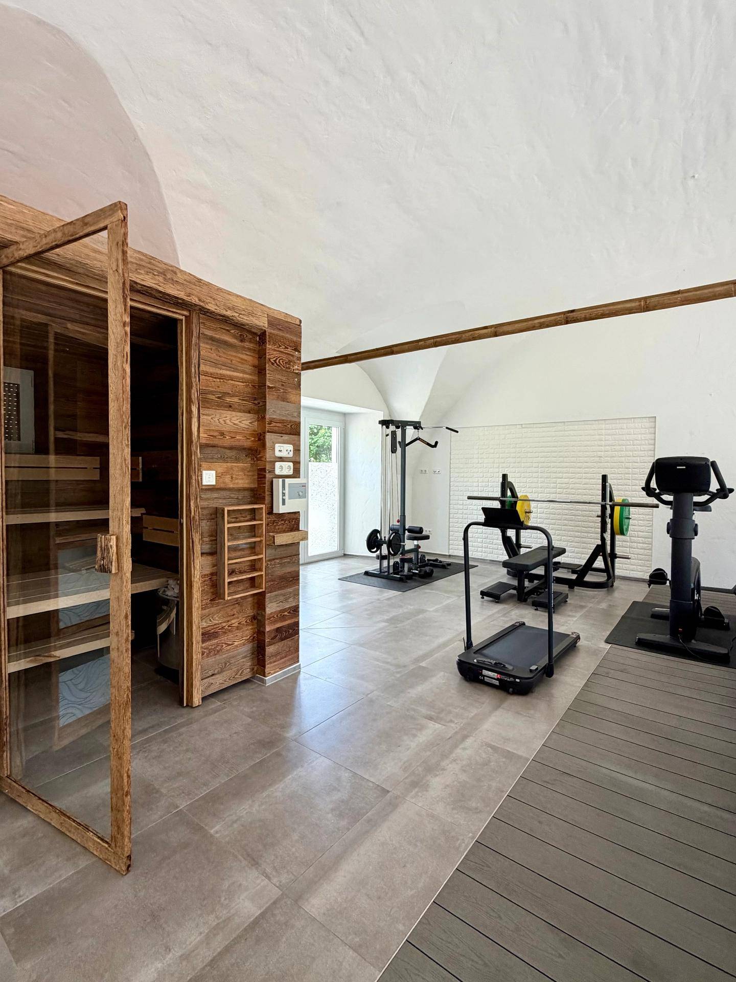 Geräumiger Fitnessraum mit moderner Sauna und verschiedenen Trainingsgeräten unter einem Gewölbedach.