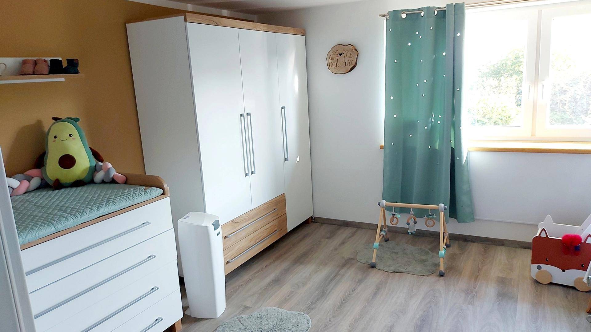 Freundliches Kinderzimmer mit Wickelkommode, Kleiderschrank und Spielzeug in hellen Farben.