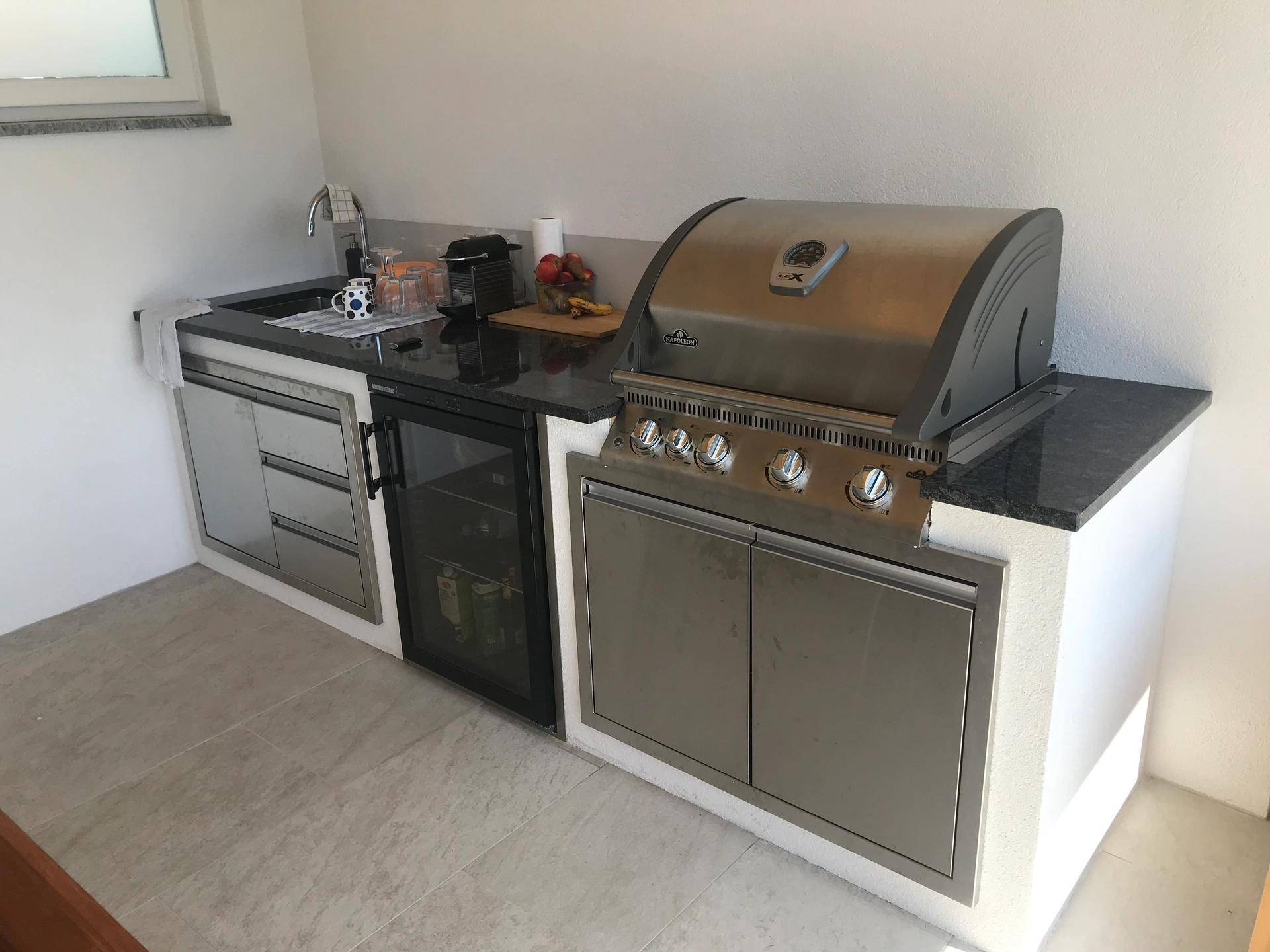 Detailansicht der modernen Außenküche mit integriertem Grill, Spüle und Kühlschrank.