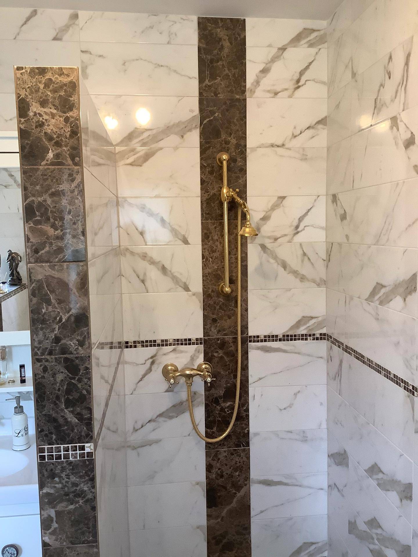 Duschbereich im Badezimmer mit luxuriösen Marmorfliesen und goldfarbenen Armaturen.