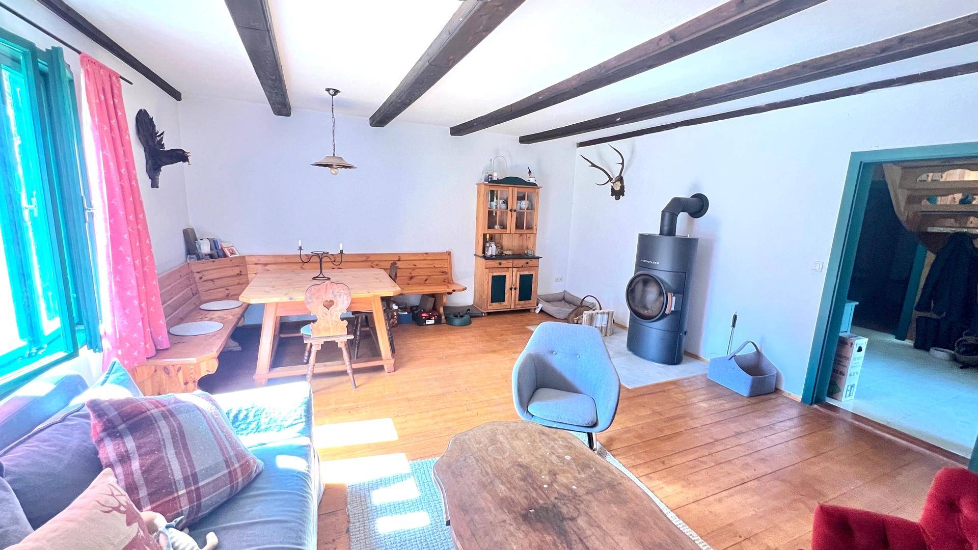 Gemütlicher Wohn-Essbereich mit Holzboden, Kaminofen und traditionellen Holzmöbeln, ideal für gesellige Stunden.