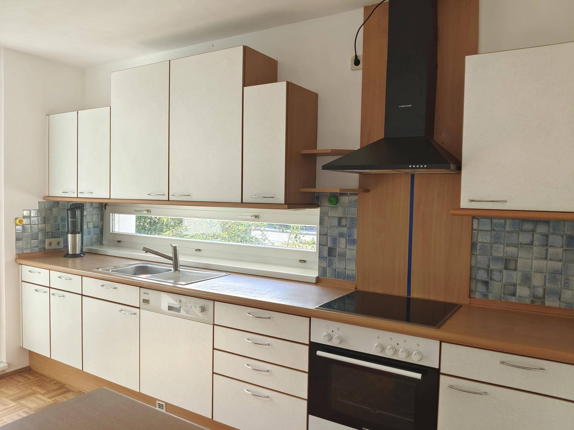 Helle Küche mit Fenster, Spülbecken, Kochfeld und ausreichend Stauraum in den Oberschränken.