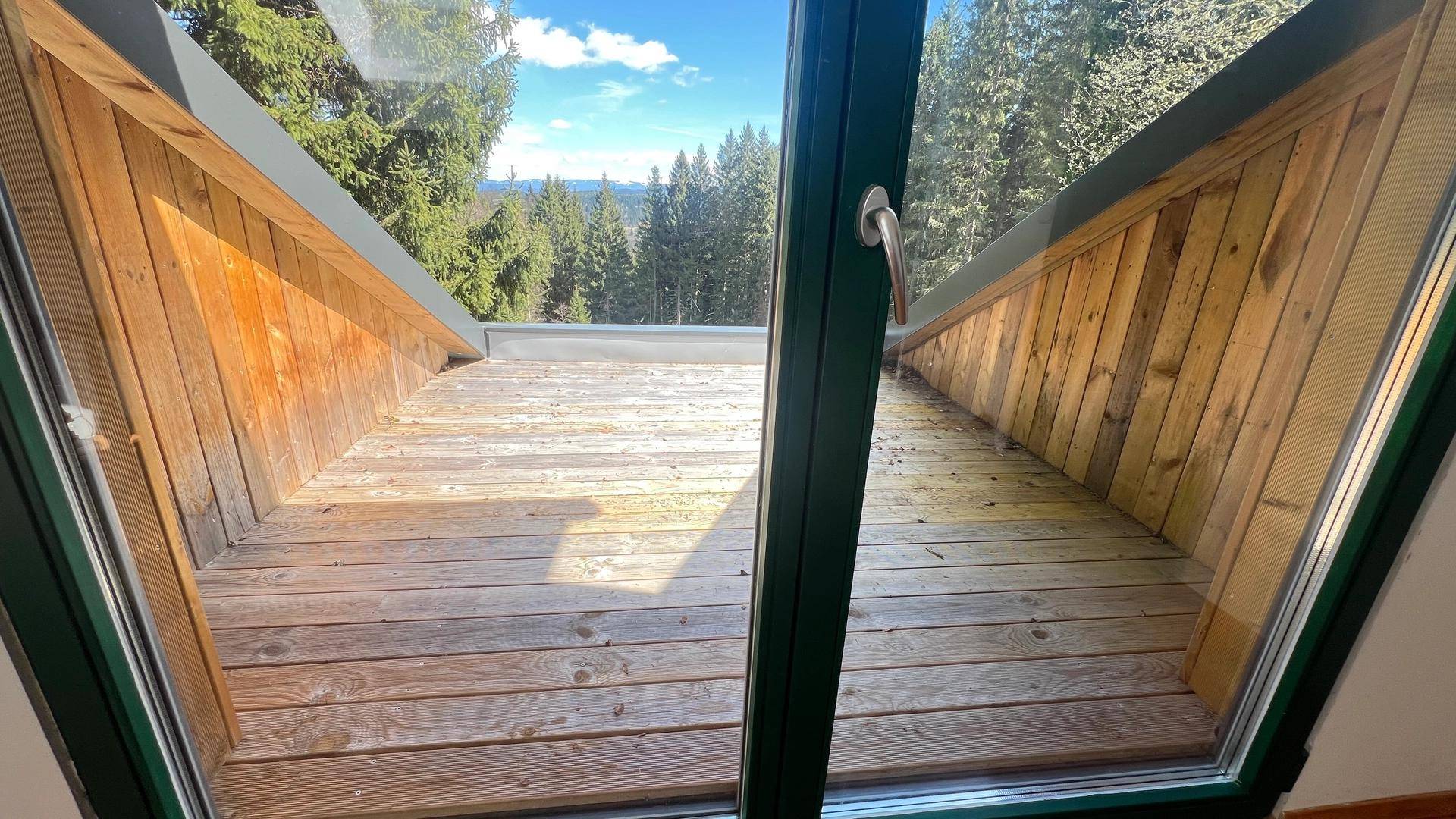 Blick vom Dachgeschoss auf eine kleine Holzterrasse mit weitreichender Aussicht ins Grüne.