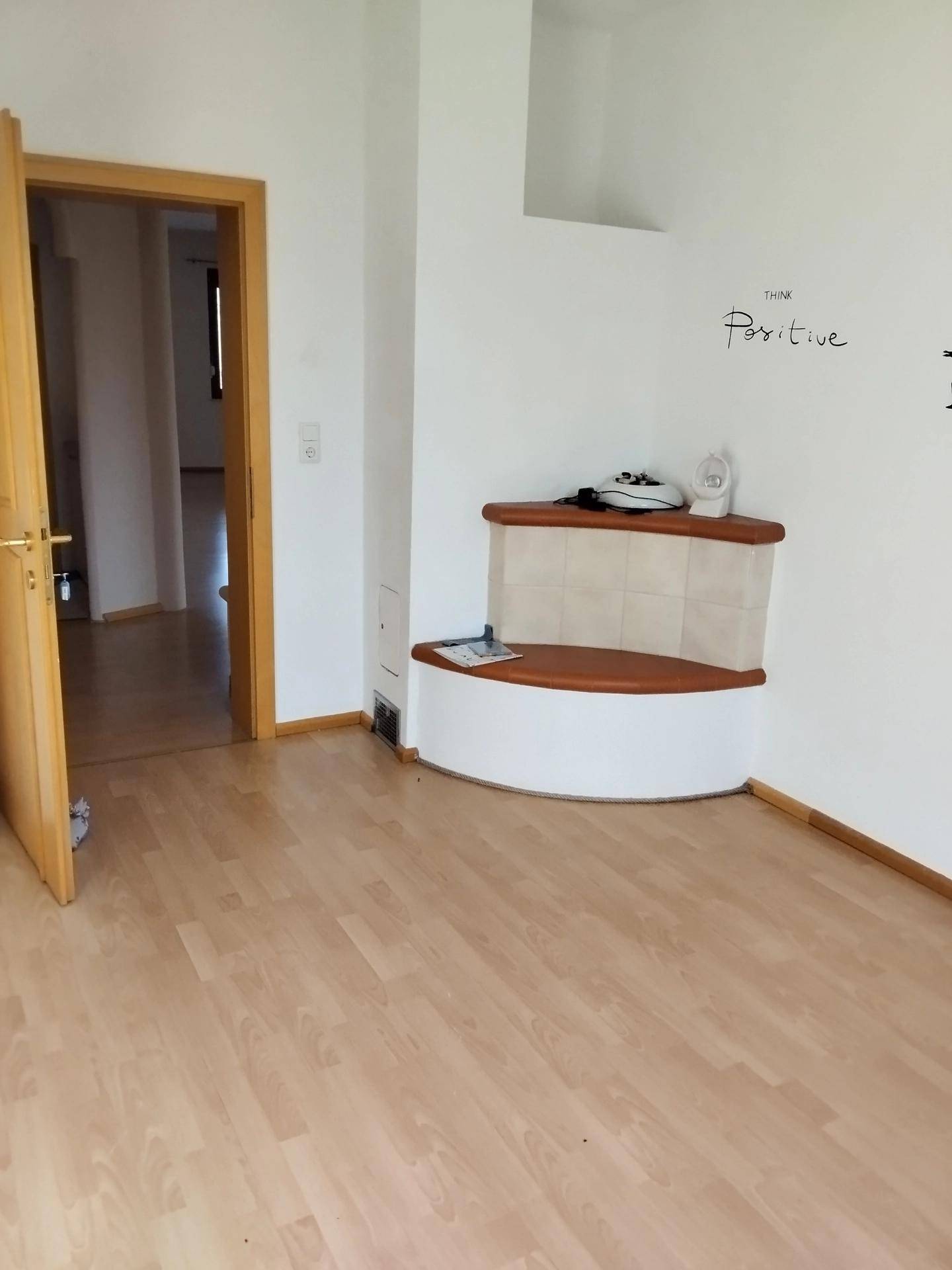Heller Raum mit Laminatboden und einem traditionellen Kachelofen in der Ecke.