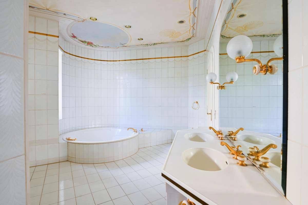 Luxuriöses Badezimmer mit großer runder Badewanne, Doppelwaschbecken und goldenen Armaturen.