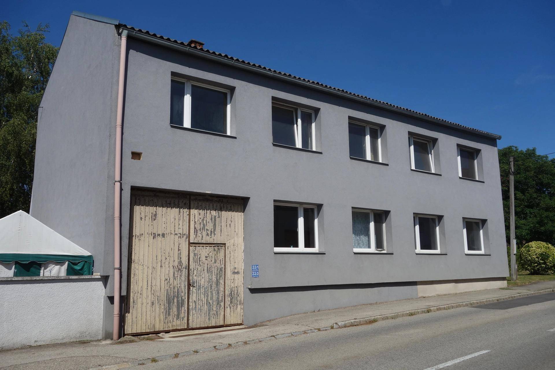 Seitenansicht des grauen Gebäudes mit Holztür und einem kleinen Zelt im Vordergrund.